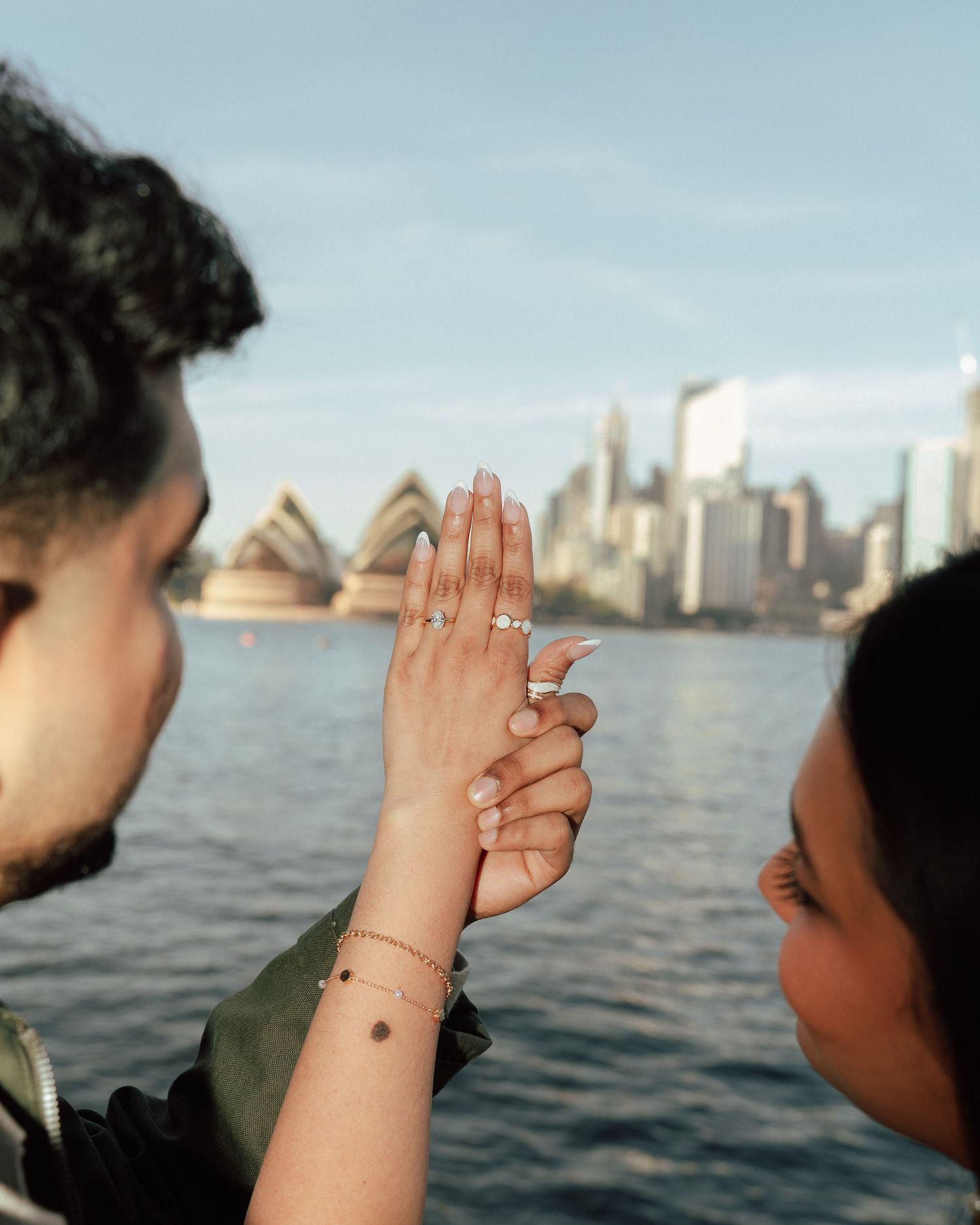 Couple showing off engagement ring with Sydney Opera House and harbor skyline in the background.