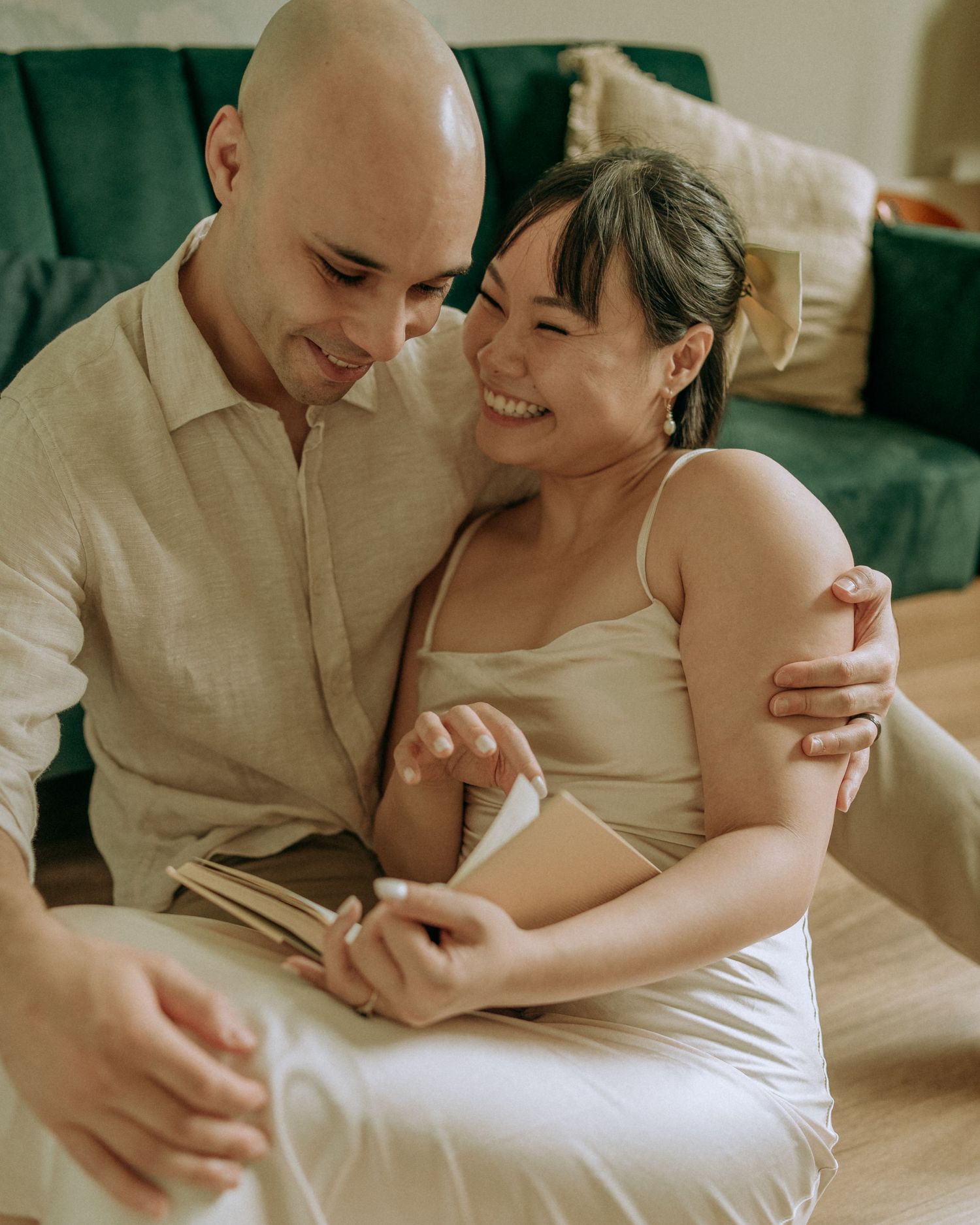 Smiling couple sitting on floor embracing and reading together near green sofa.