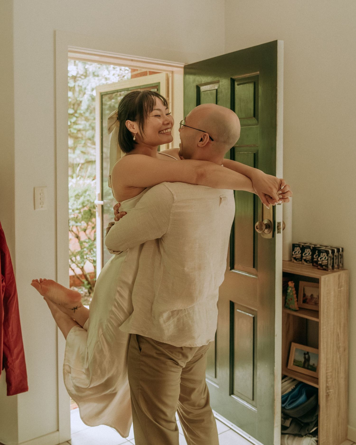 Joyful couple embracing near a green door, man lifting woman as she laughs with legs raised.