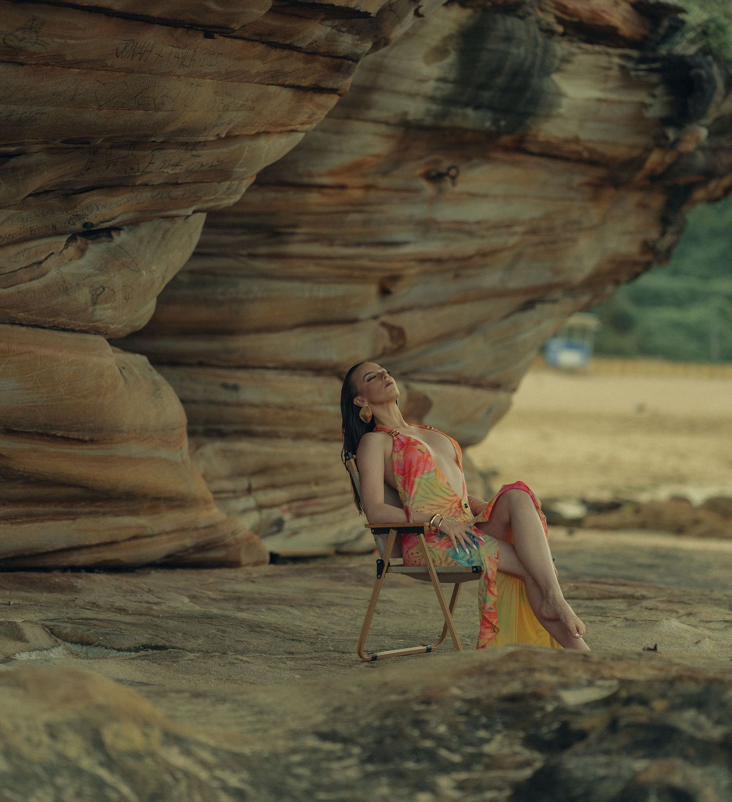 Woman in colorful floral dress relaxing on a chair beside large sandstone rocks.
