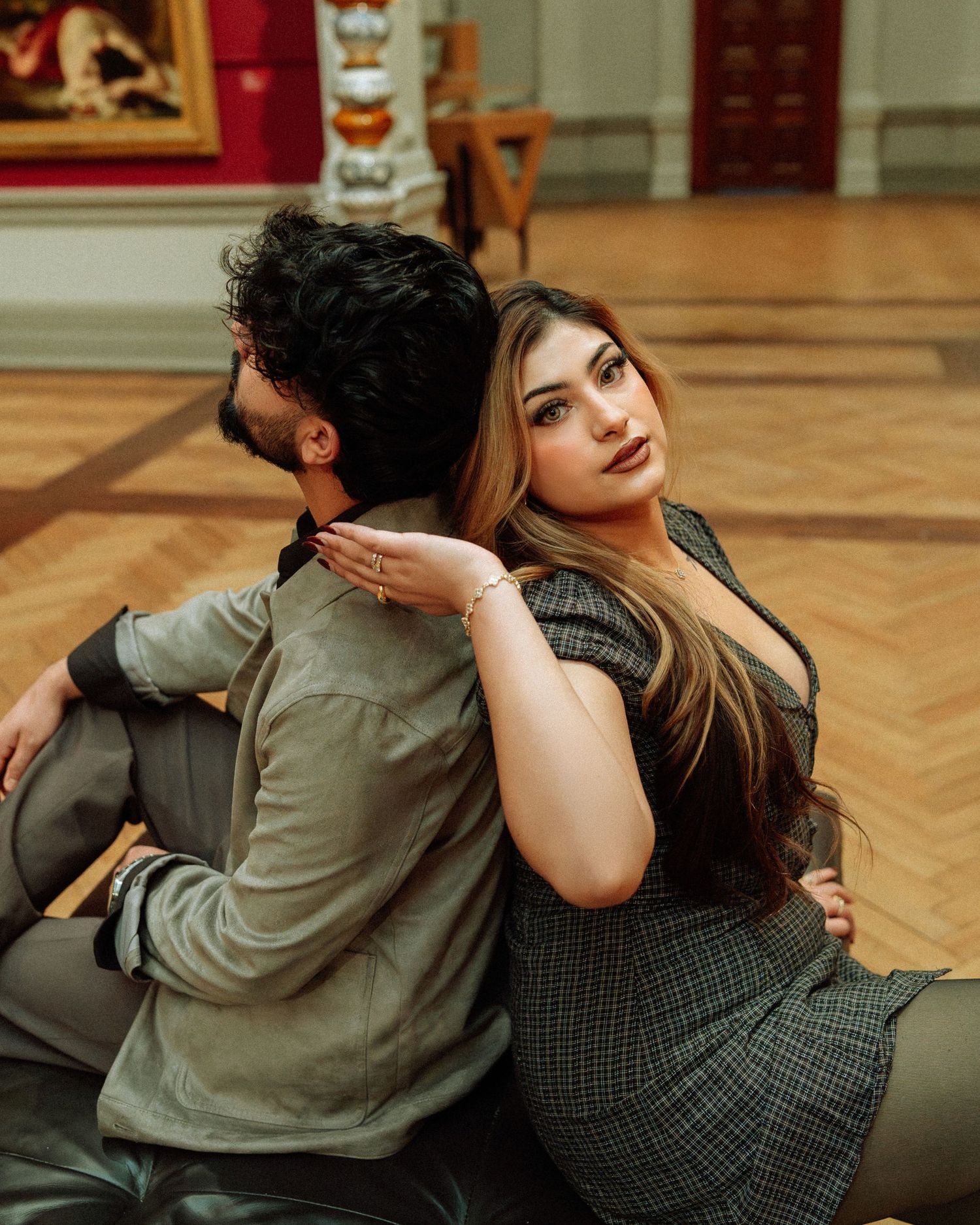Couple sitting back to back on floor of a classic art museum gallery.