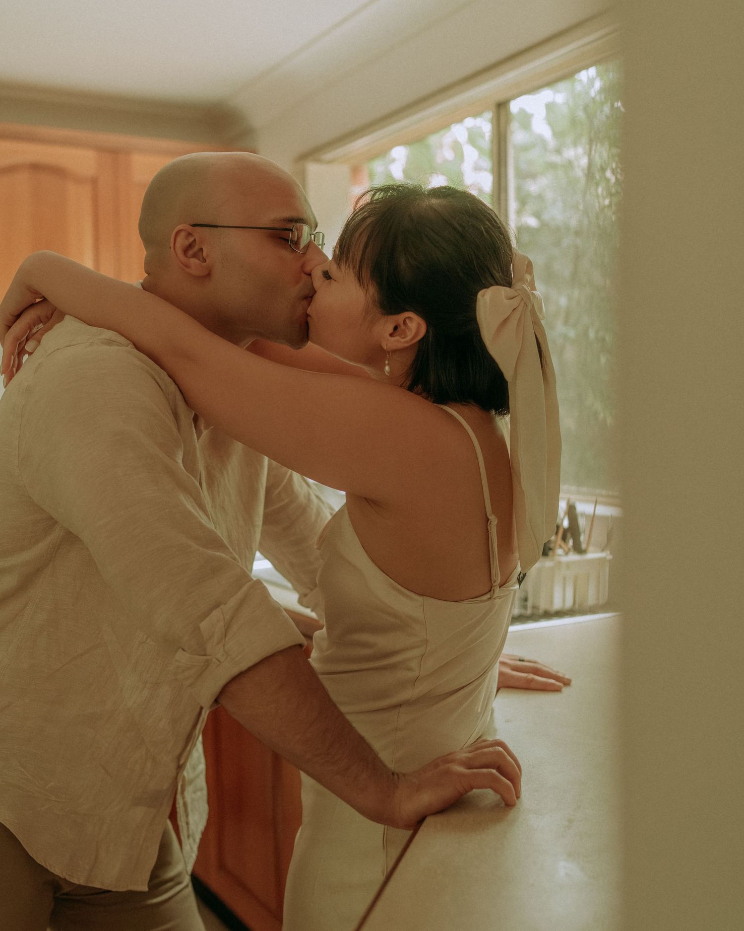 Couple sharing a passionate kiss leaning against kitchen counter in warm toned intimate home setting.