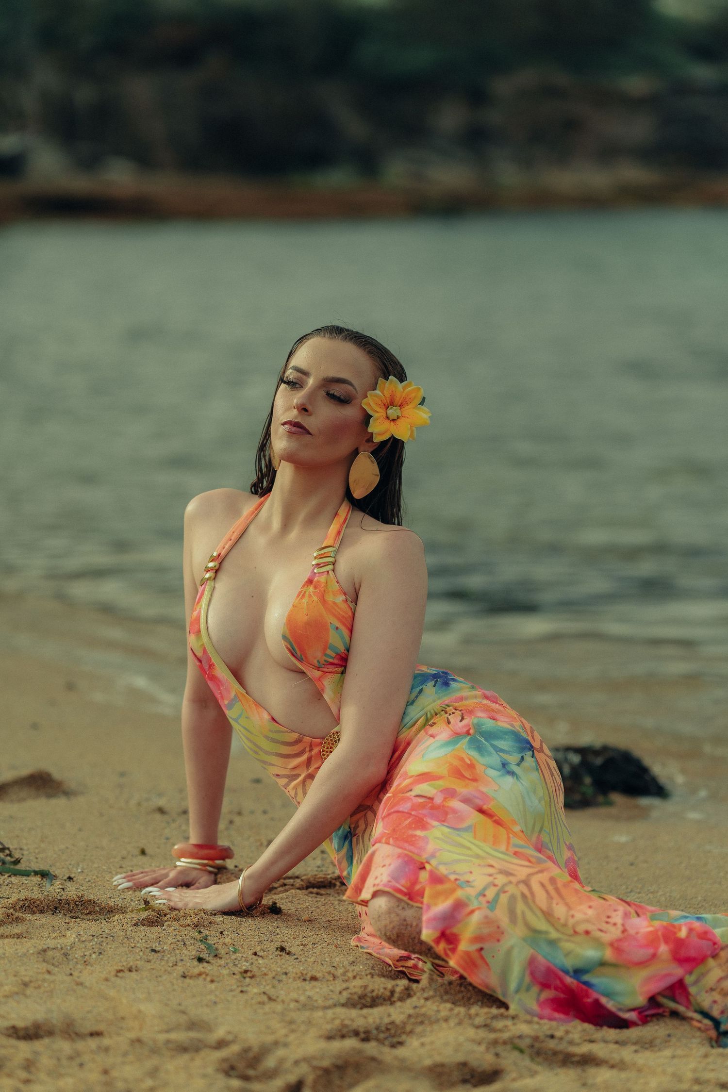 Woman in colorful floral bikini top and skirt sitting gracefully on sandy beach with eyes closed.