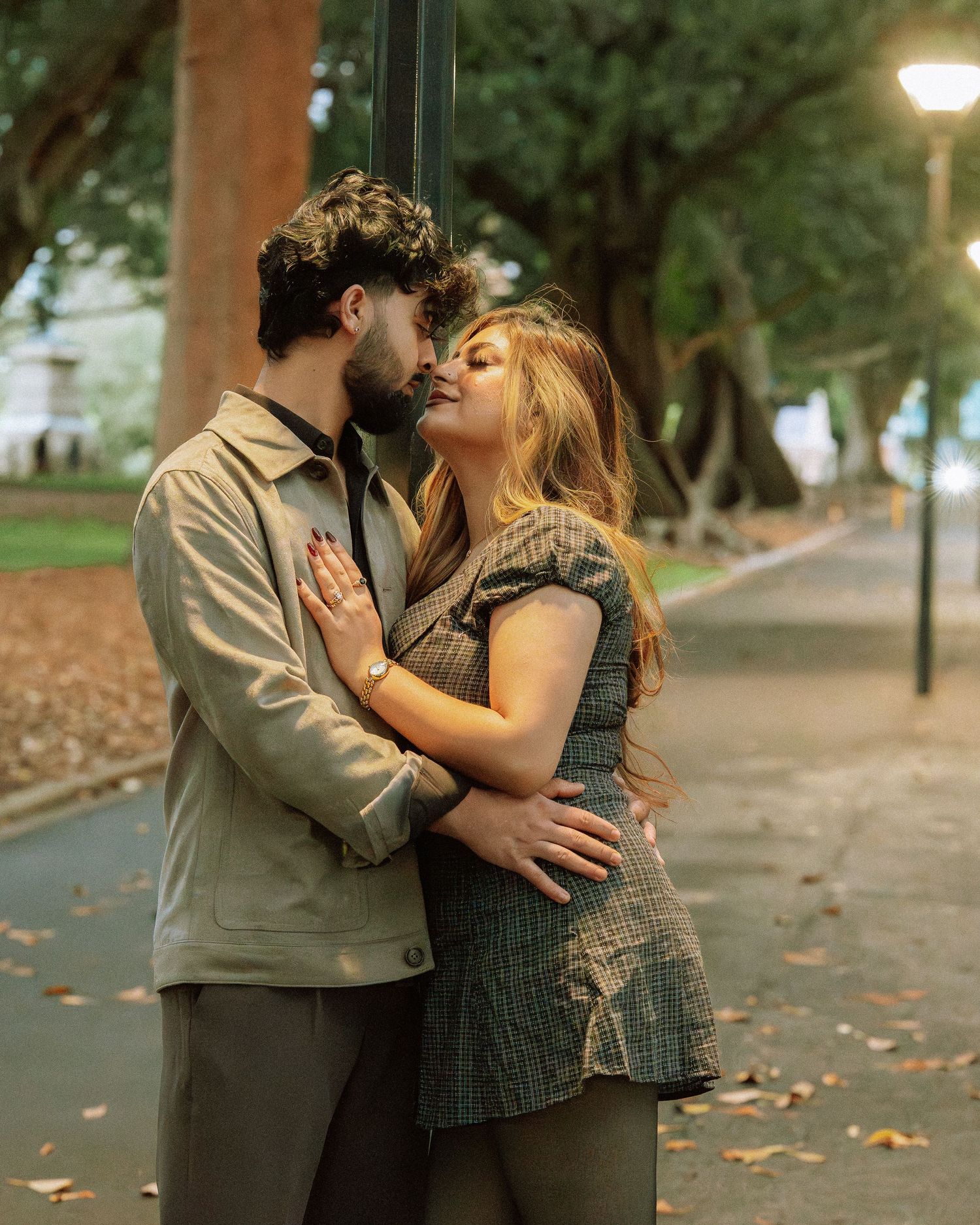 Couple sharing a tender kiss near a glowing street lamp in an autumn park.