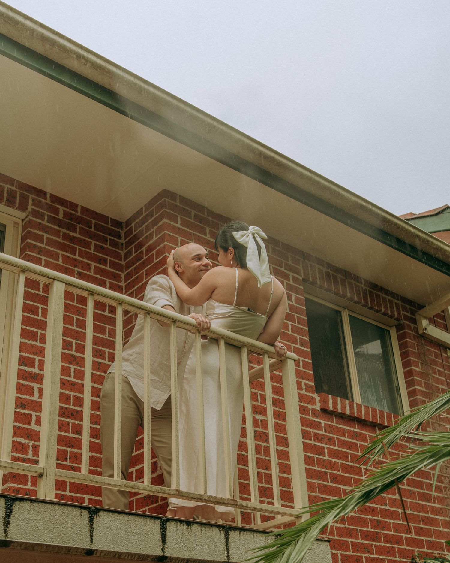 Couple sharing a romantic kiss on balcony of classic red brick apartment building.