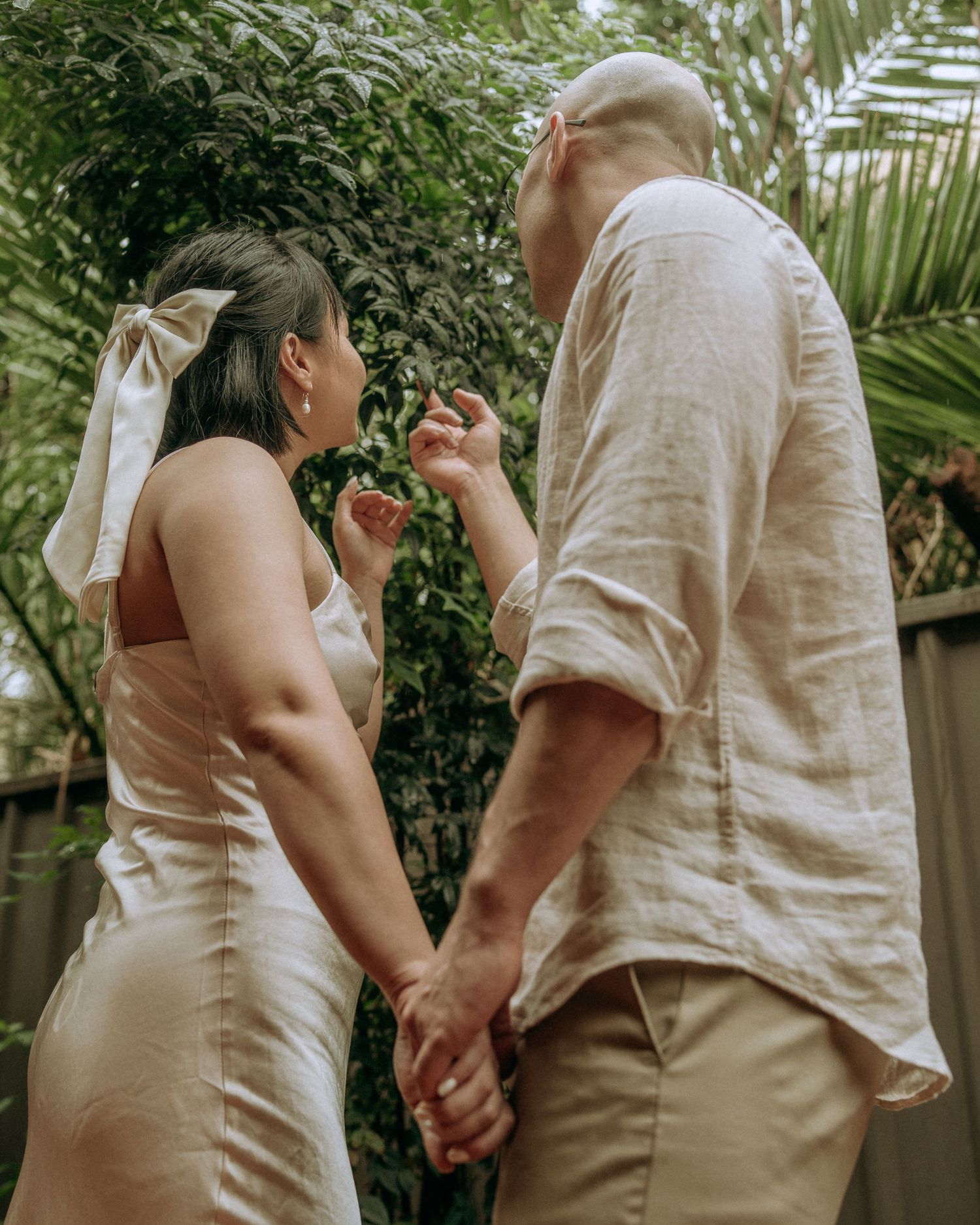 Couple holding hands and sharing a playful moment among green garden foliage.