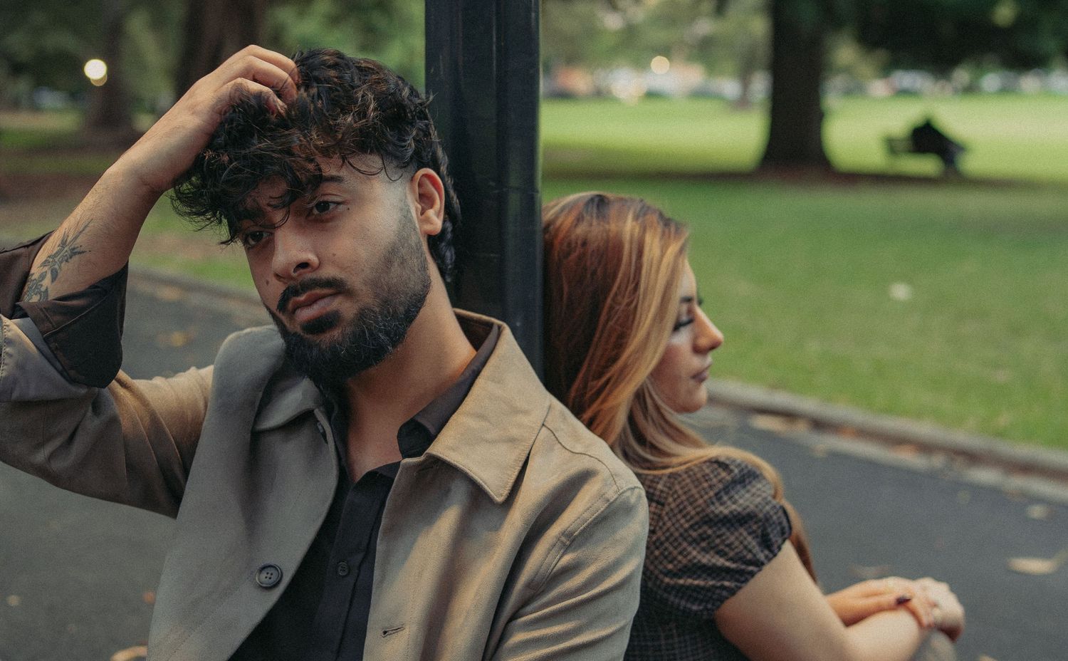 Couple sitting apart on a park bench looking upset, suggesting relationship tension outdoors.