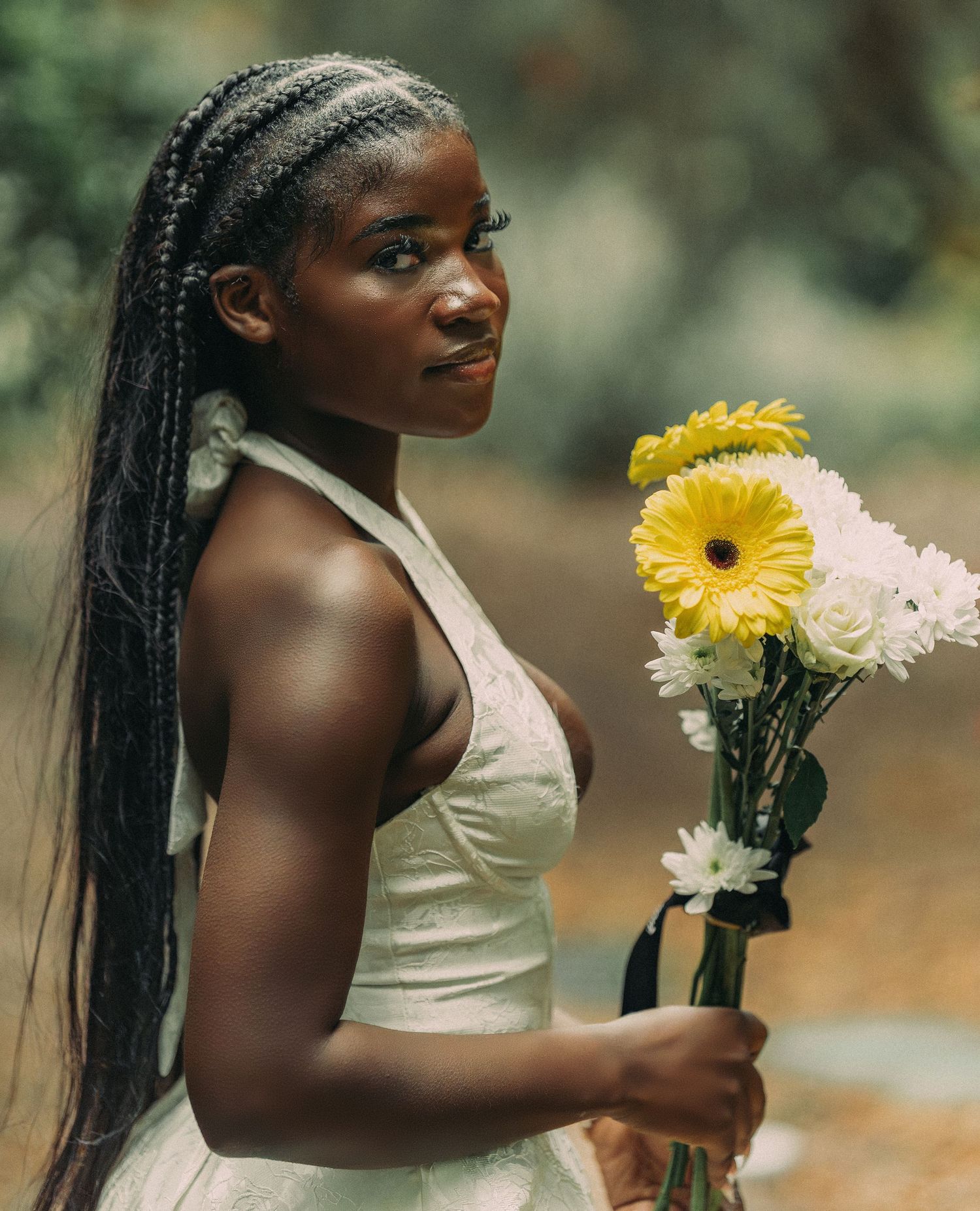 Young Black woman with braided hair holds bouquet of yellow and white flowers in outdoor portrait.