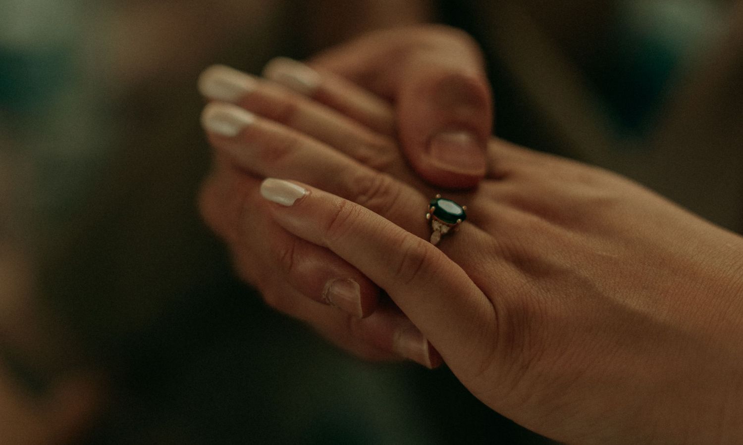 Close-up of hands with engagement ring featuring dark gemstone and white nails.