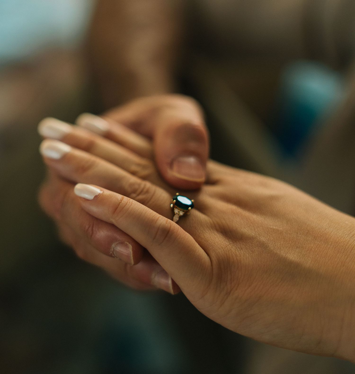 Close-up of hands holding, woman wearing a dark gemstone engagement ring with white nails.