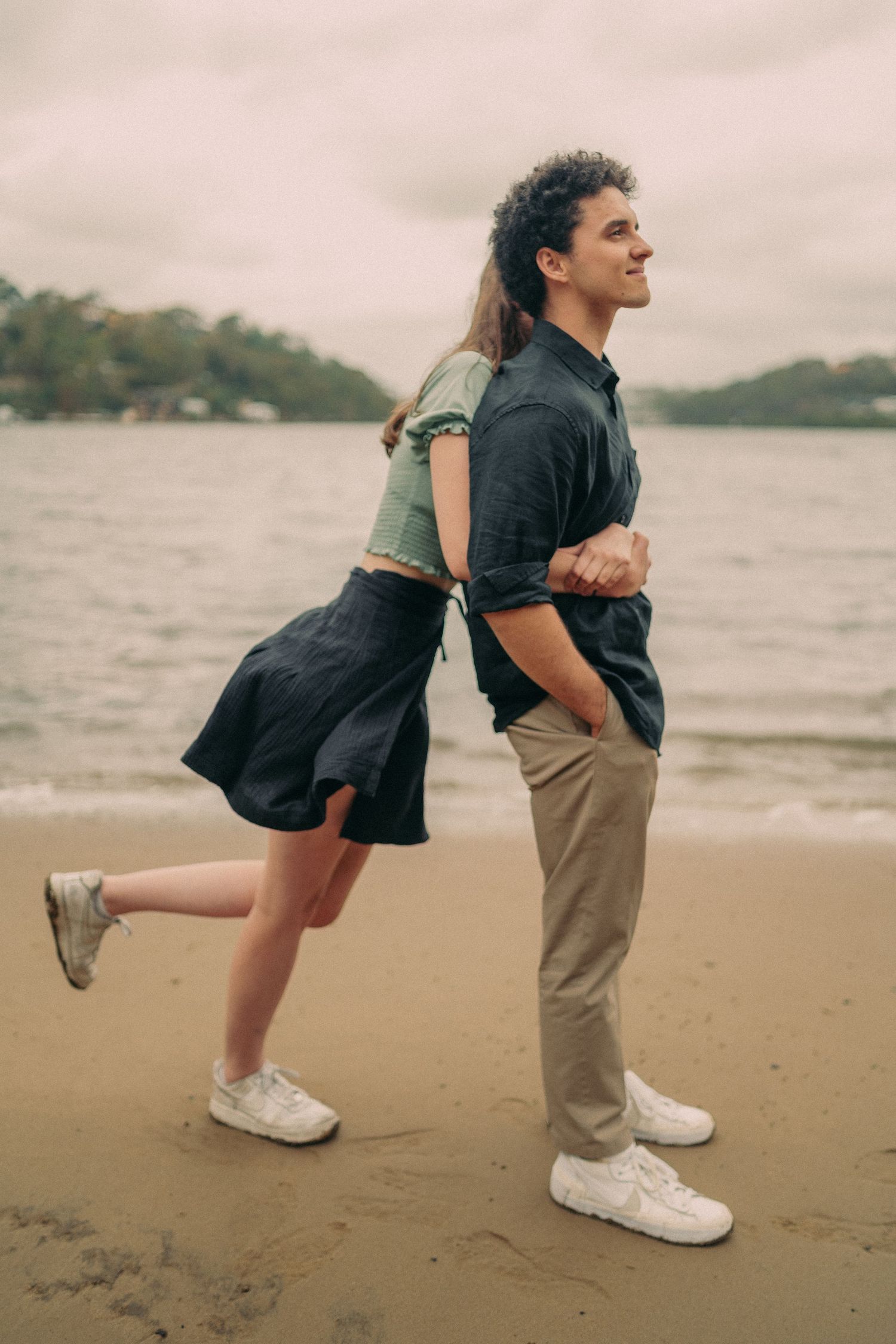 Romantic couple embracing on a sandy beach, woman leaning back into mans arms with ocean backdrop.