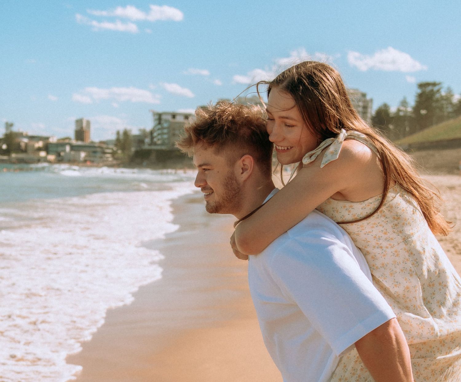 Happy couple at the beach, woman piggyback riding on mans back near the ocean shore.