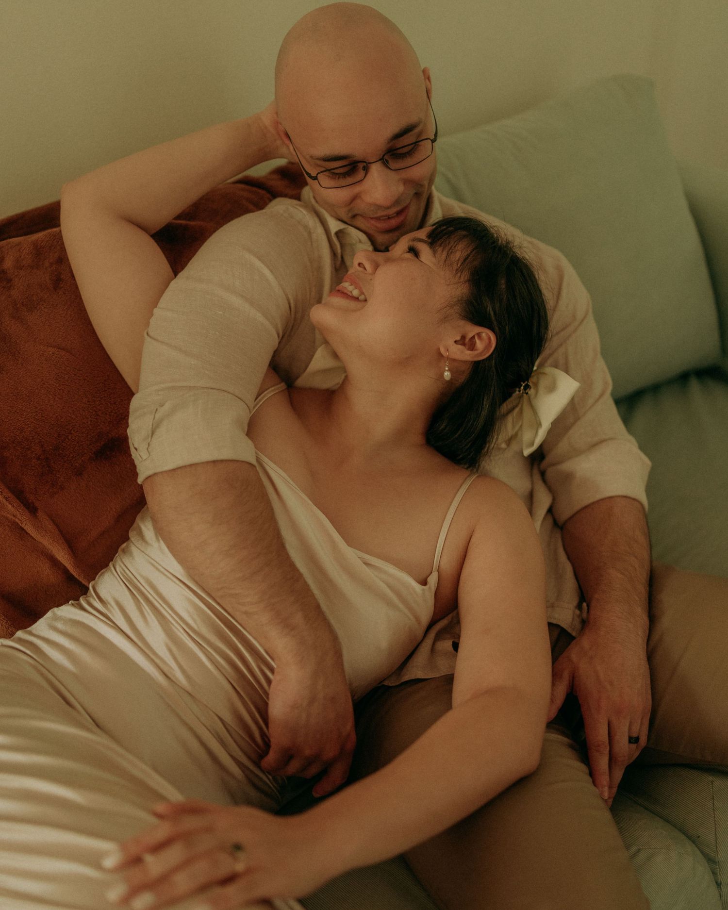 Couple relaxing on couch together, woman laughing while leaning back on man.