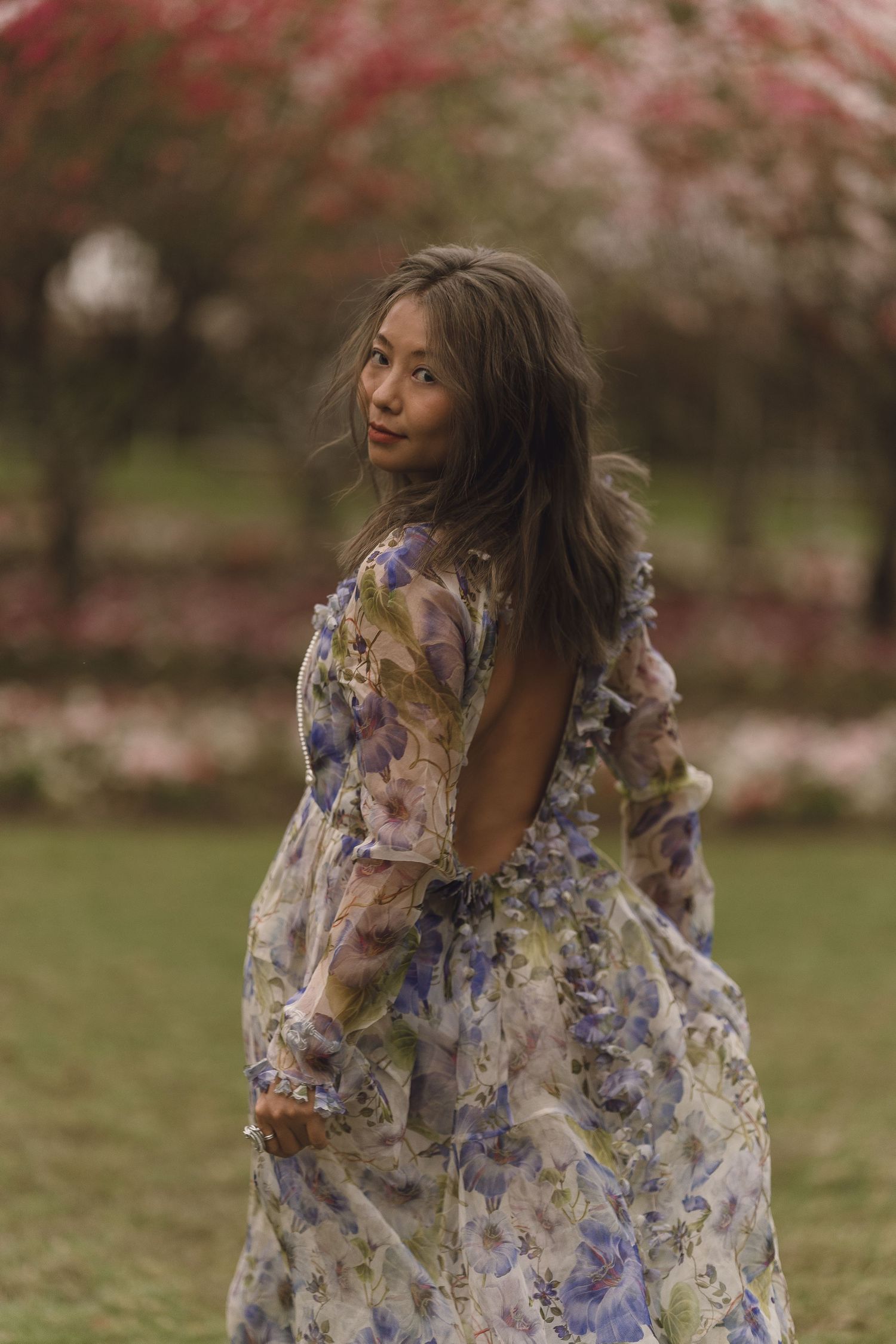 Woman in backless floral dress posing among pink blooming trees.