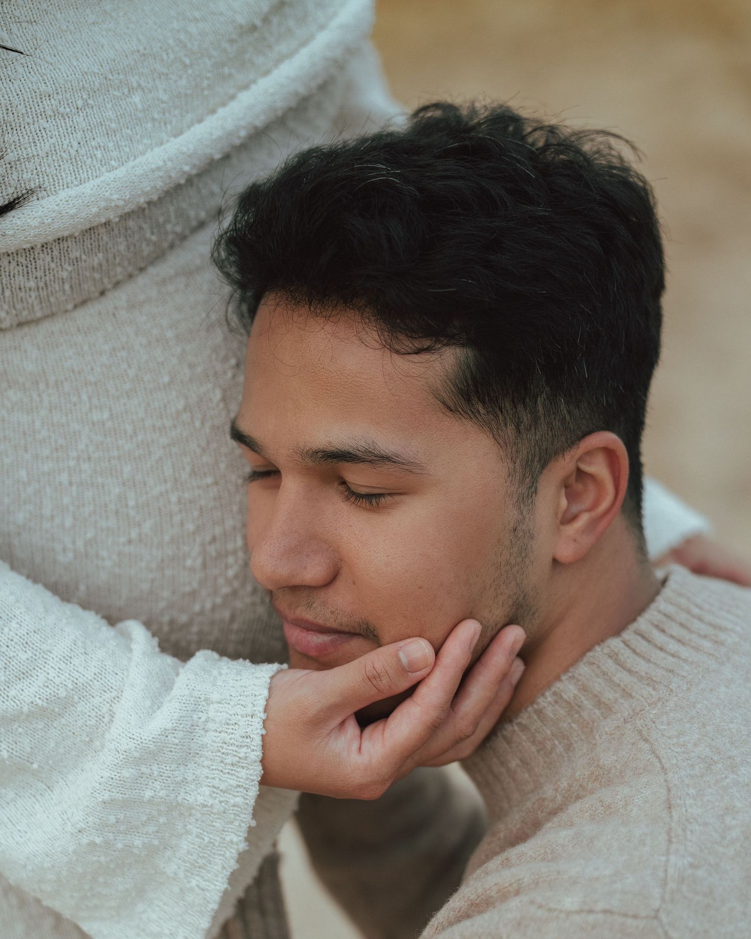 Close-up of man with eyes closed as pregnant partner gently cradles his face during intimate maternity session.