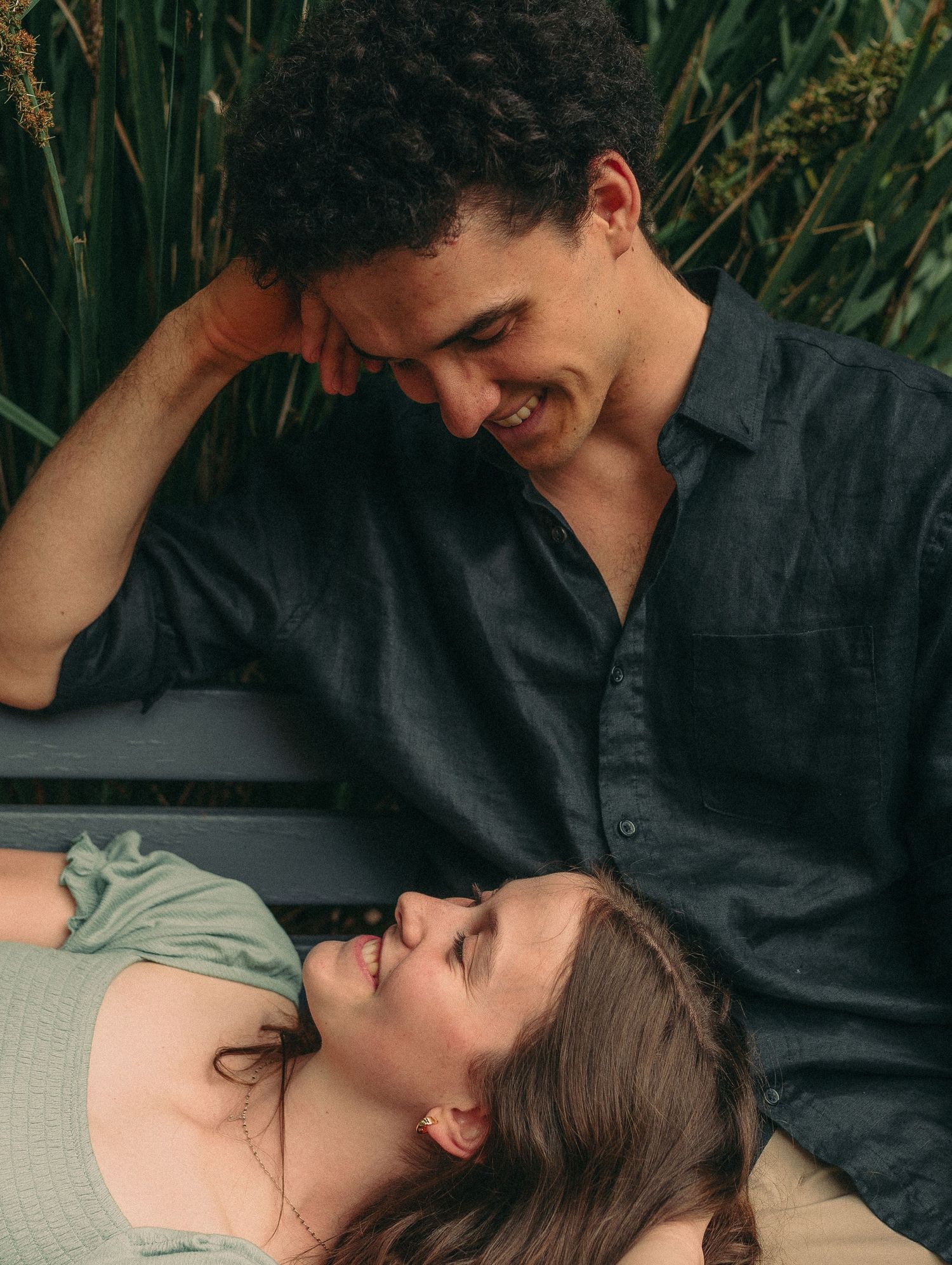 Couple sharing a tender moment on a bench, woman lying down smiling up at man.