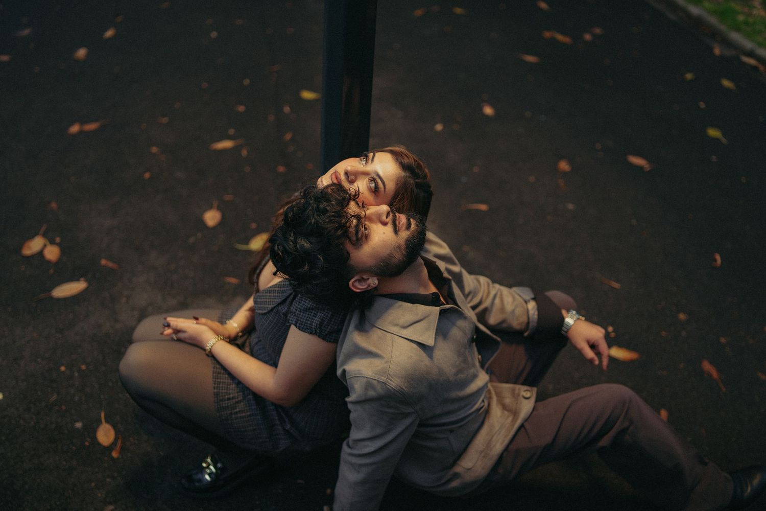 Romantic couple sitting on ground leaning against a lamp post at night.