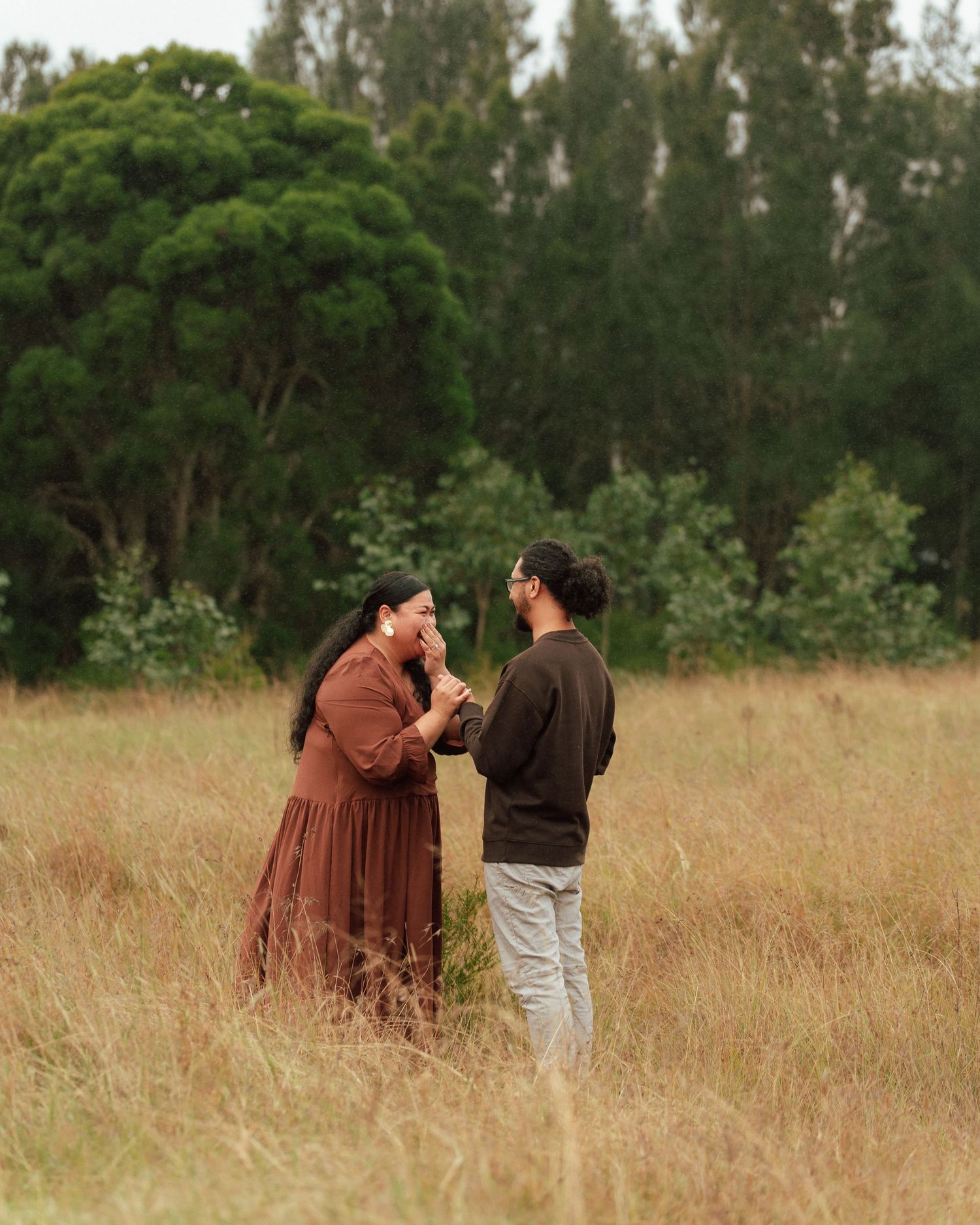 A couple shares a tender moment in a golden field, the man gently kissing the woman's hand.