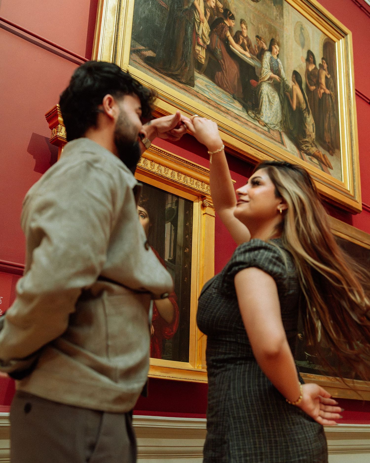 Couple admiring large classical paintings on red walls inside a grand art museum gallery.
