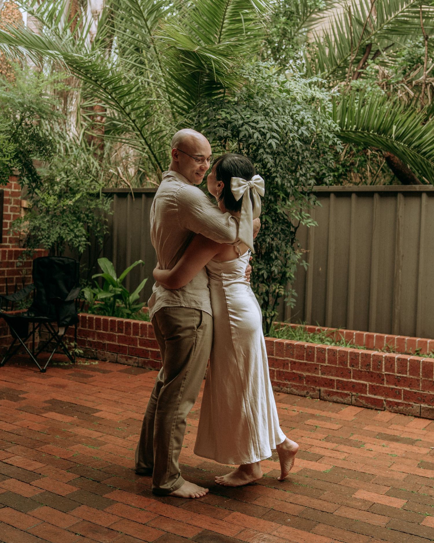 Couple sharing a warm embrace on a brick patio surrounded by lush tropical garden greenery.