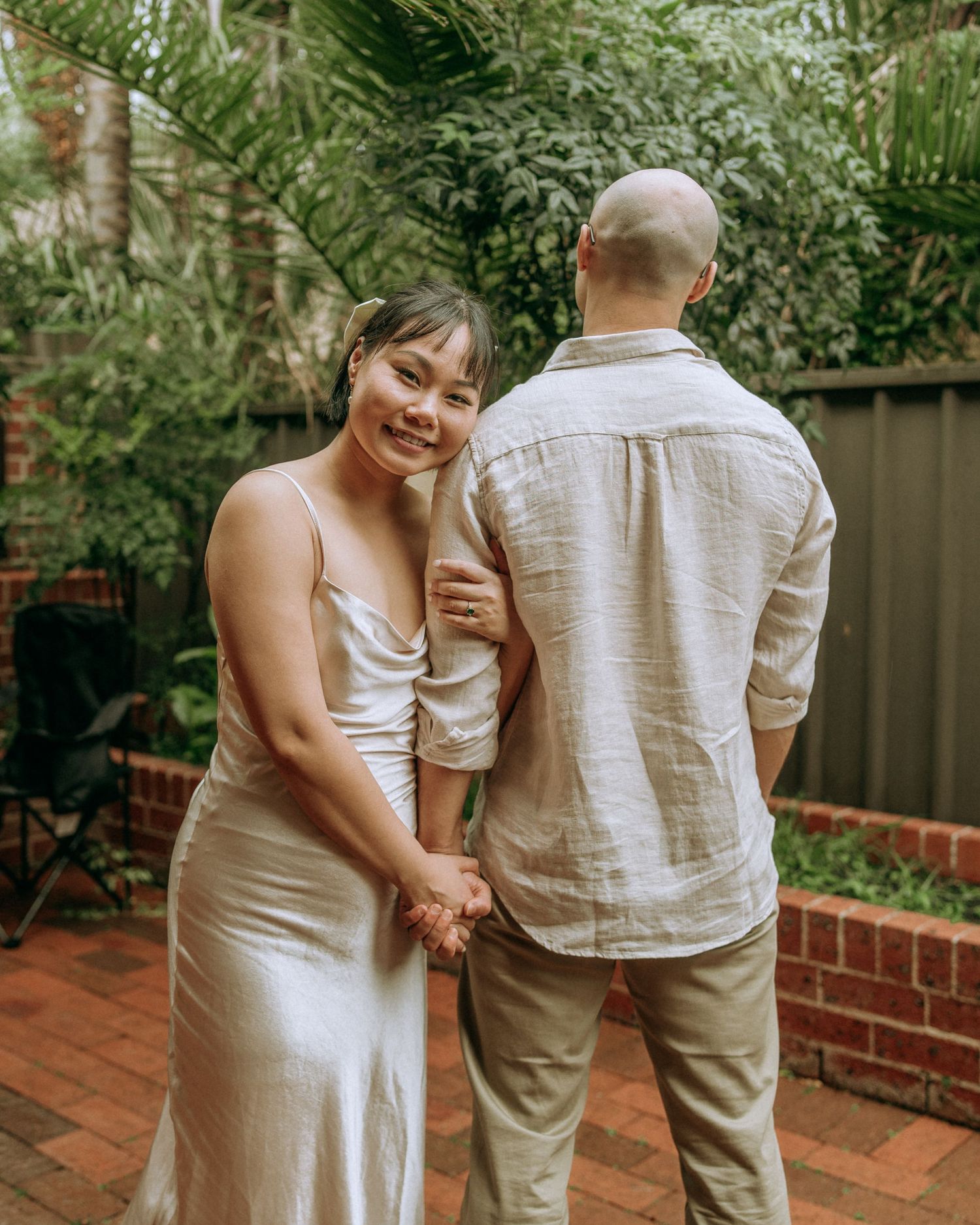 Couple holding hands on a brick patio, bride in silk dress smiling over her shoulder.