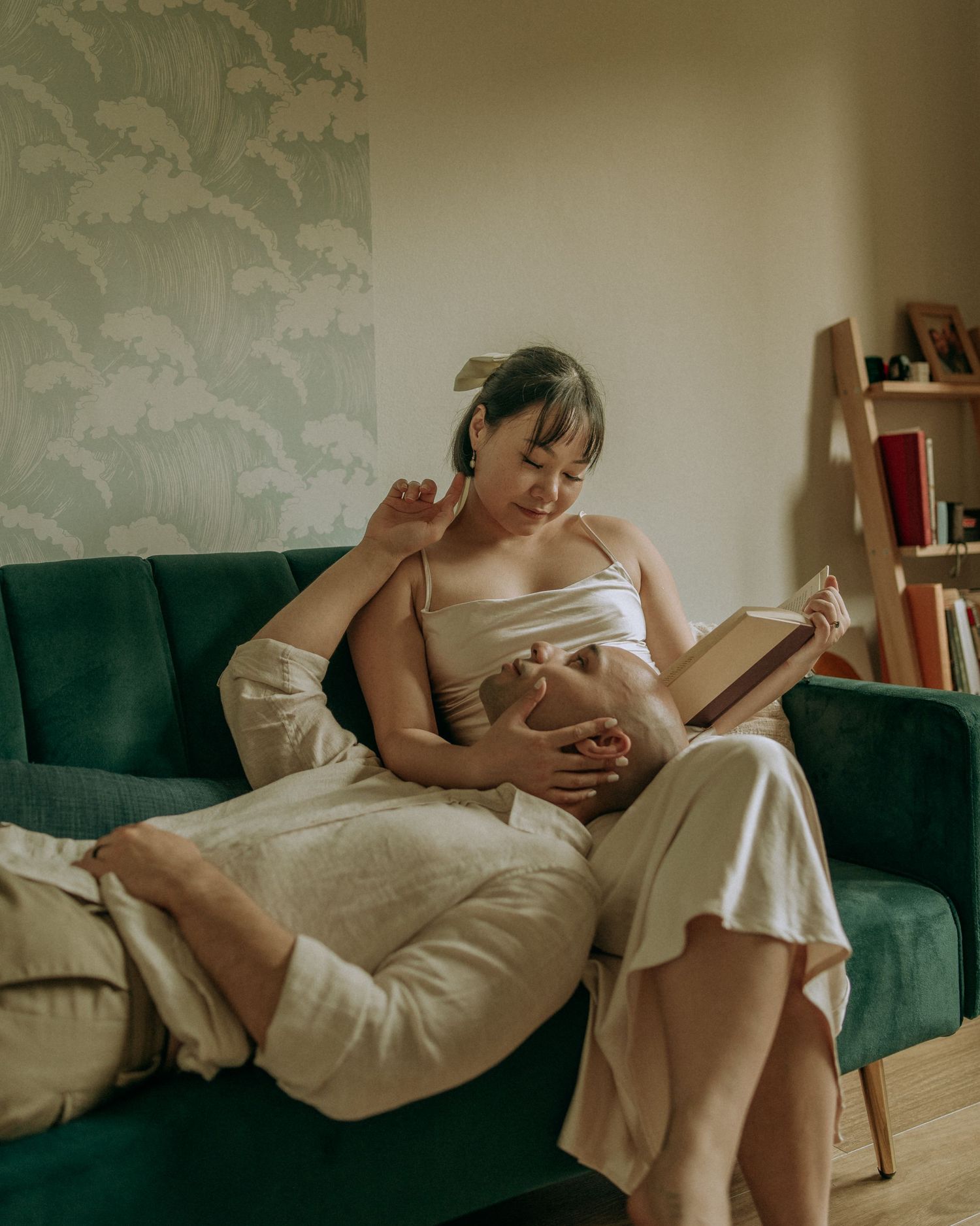 Couple relaxing on green velvet sofa reading a book together in cozy home setting.