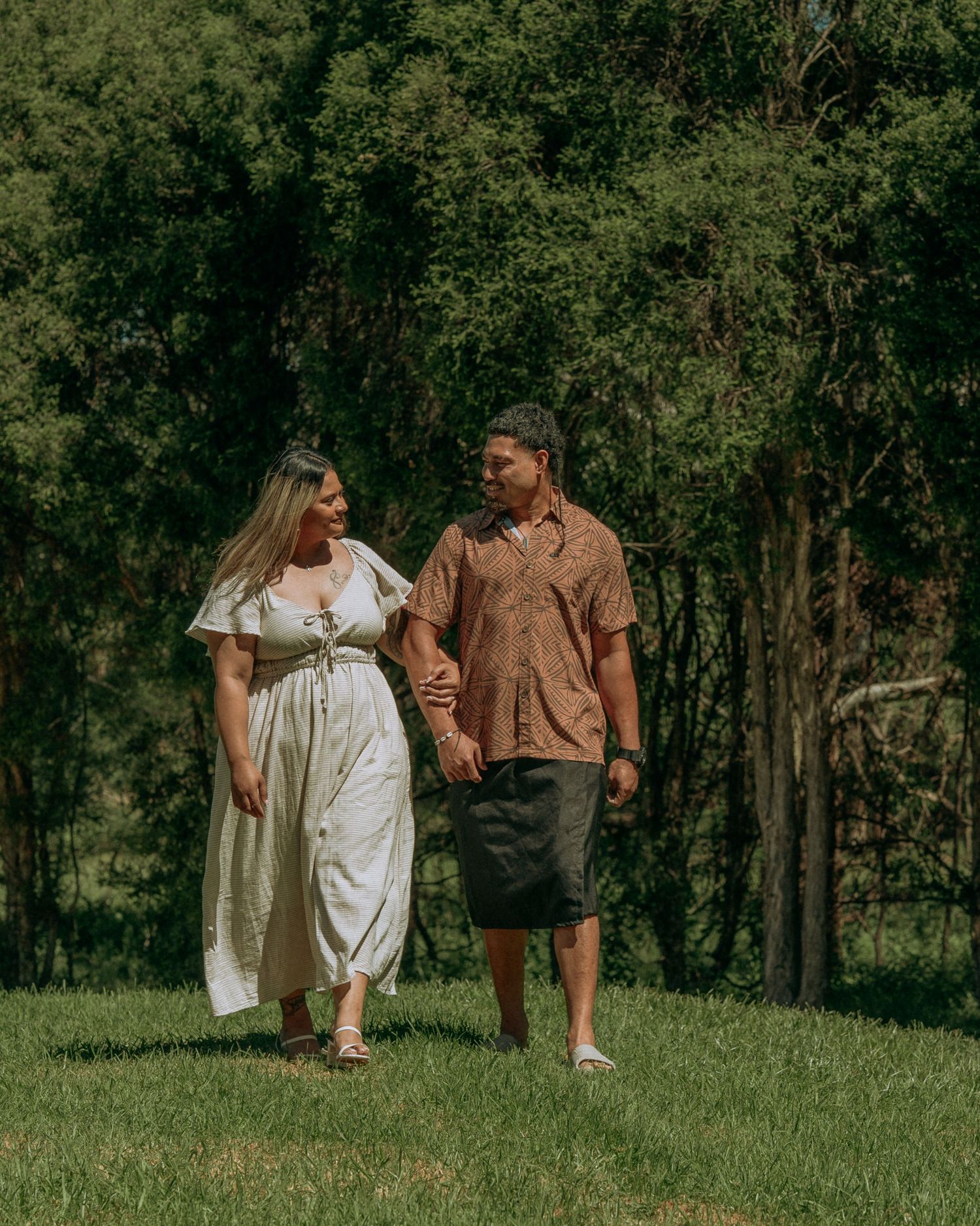 Couple walking hand in hand through green park surrounded by lush trees.