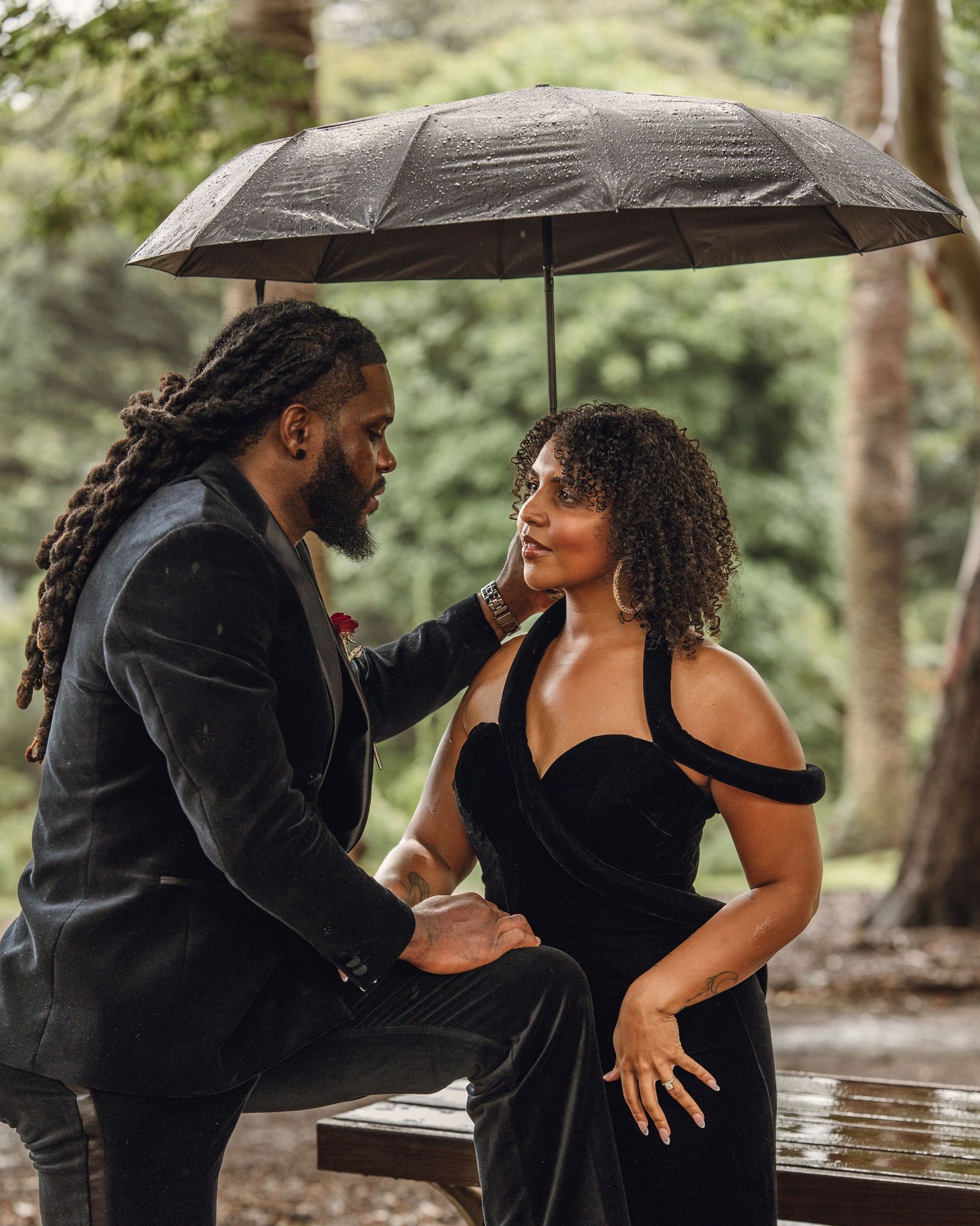 Elegant couple in black attire sharing a romantic moment under an umbrella.