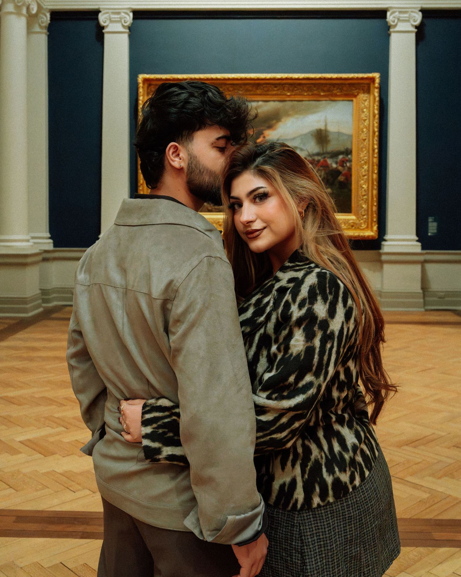 Couple posing in an art gallery, woman in leopard print top smiling over shoulder.