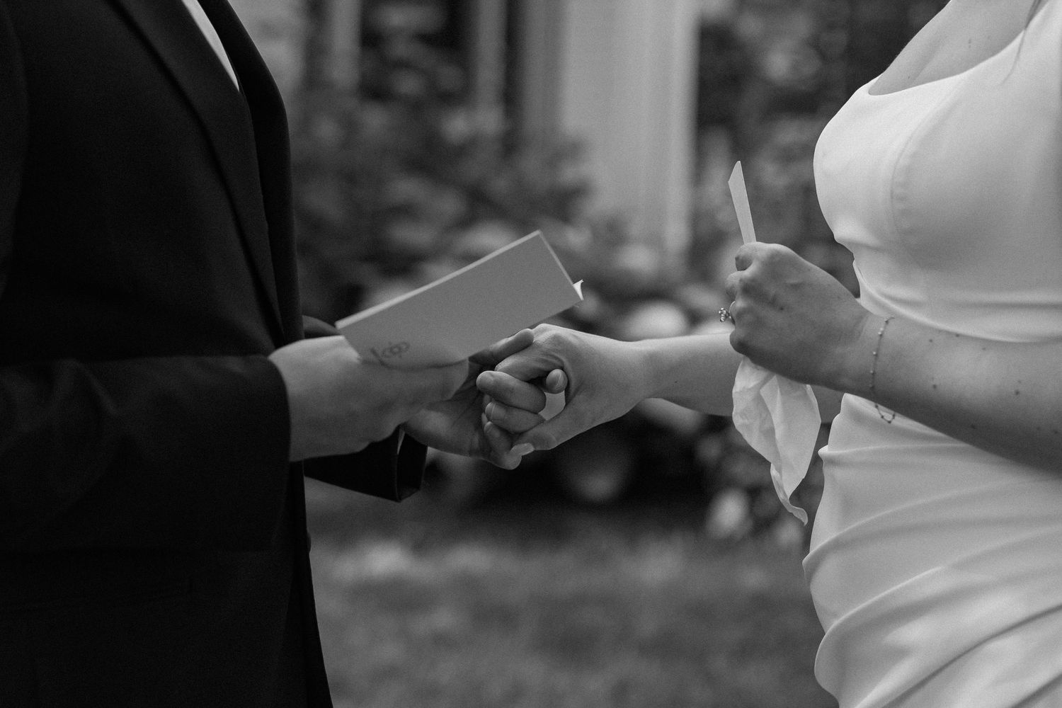 Black and white photo of bride and groom holding hands during outdoor wedding ceremony.