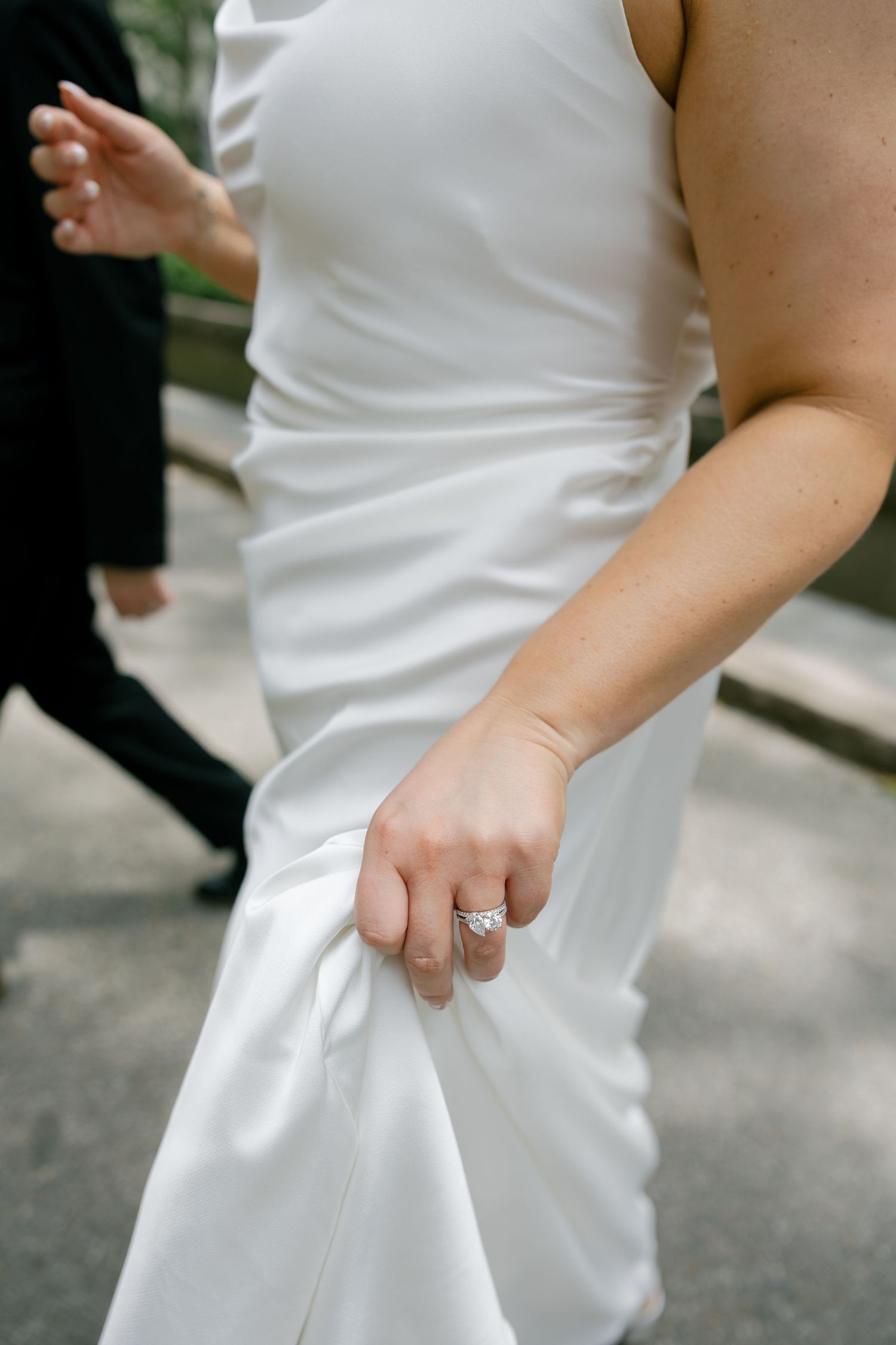Close-up of bride lifting white satin wedding dress hem showing diamond engagement ring.
