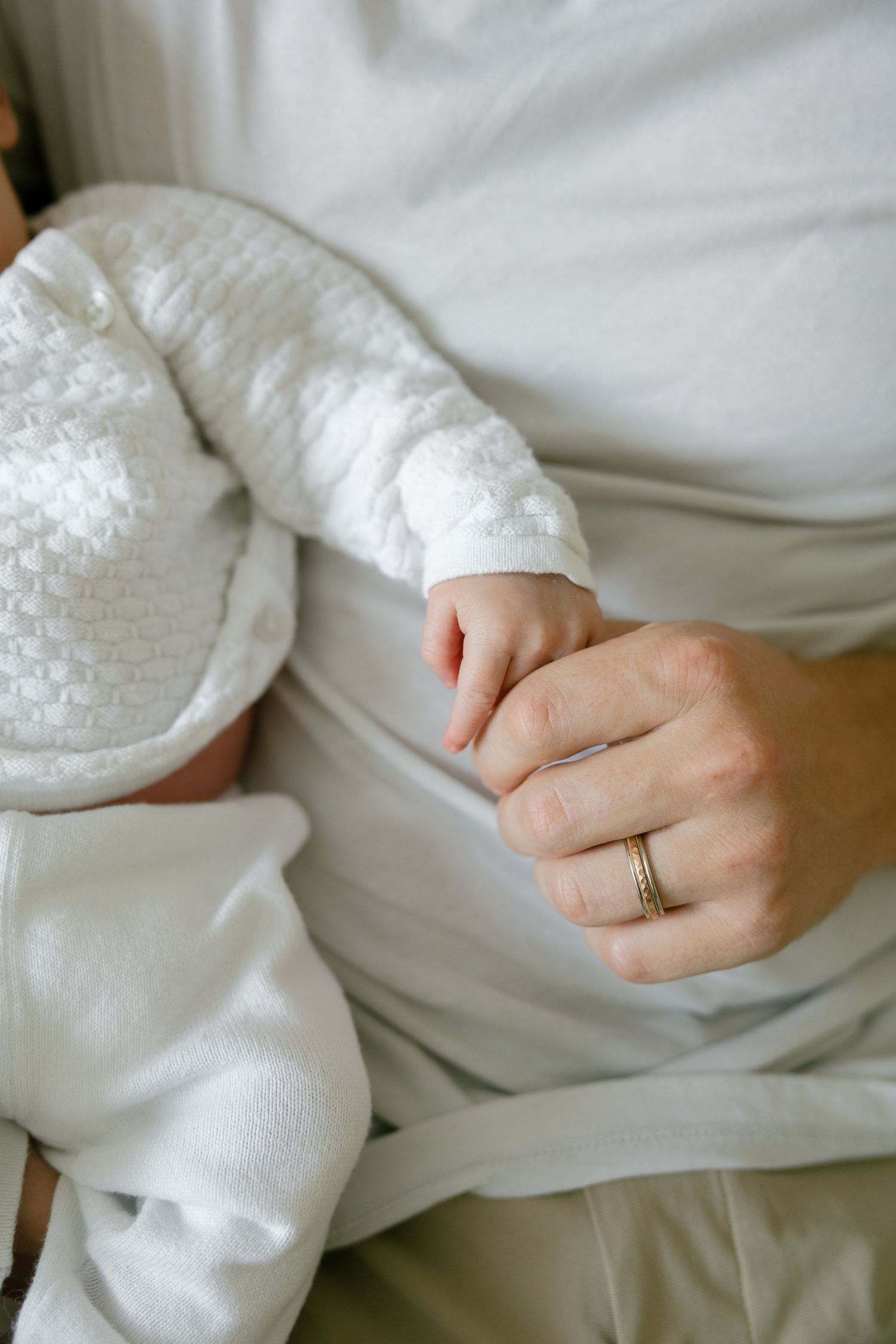 Close-up of newborn baby's tiny hand grasping parent's finger, parent wearing a gold wedding band.