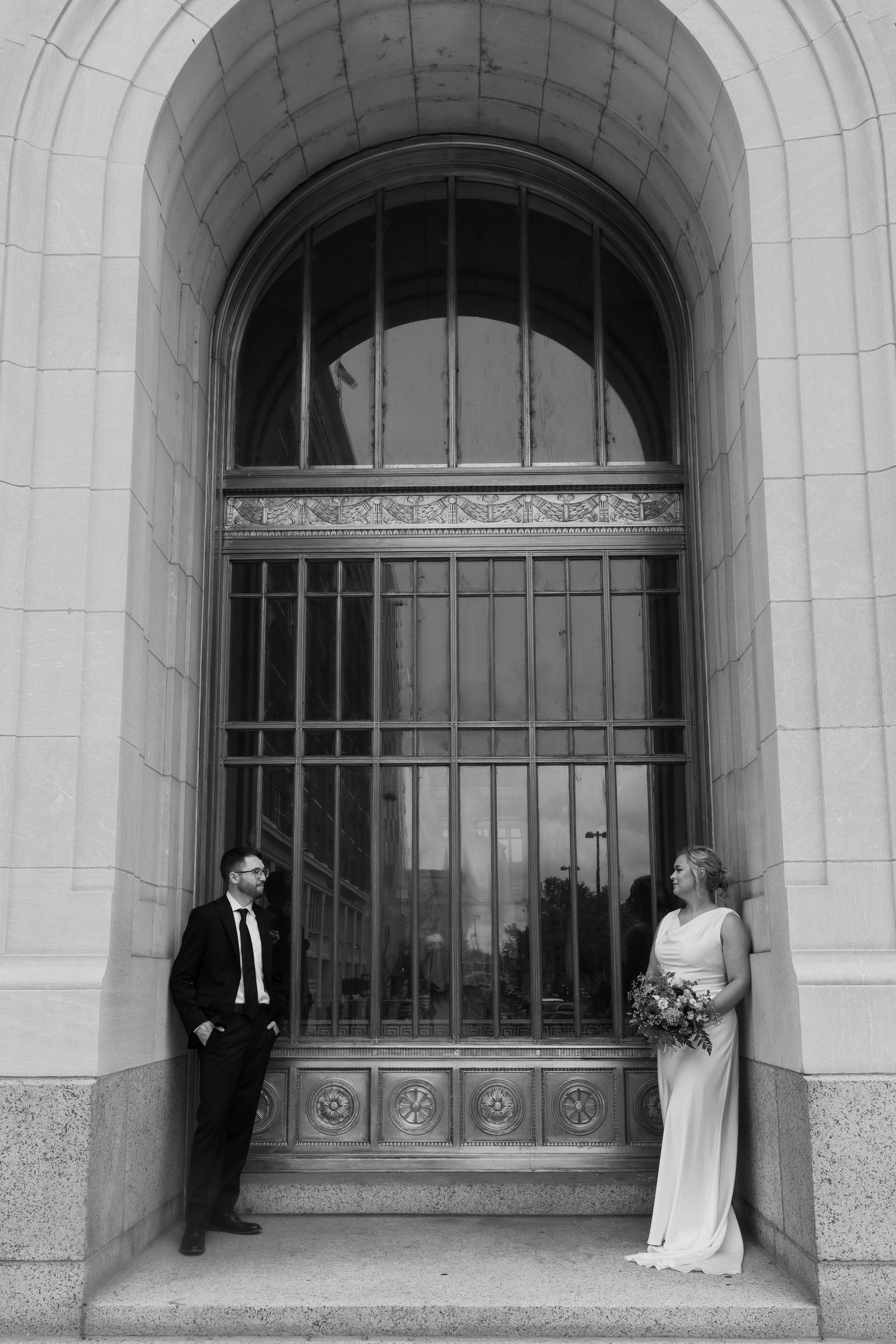 Black and white photo of bride and groom posing in arched doorway of historic building.