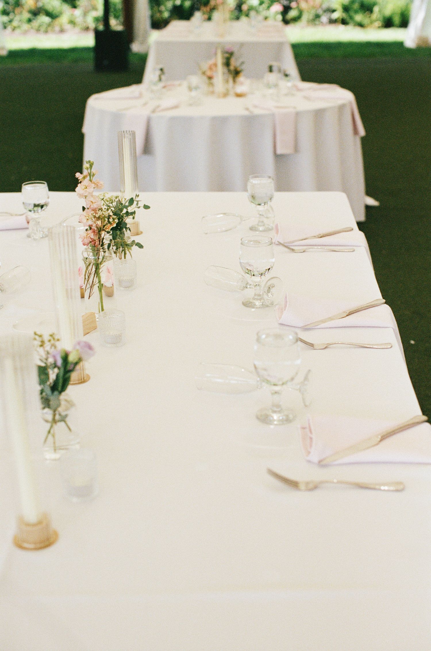 Elegantly set wedding reception tables with white linens, candles, and delicate floral centerpieces.