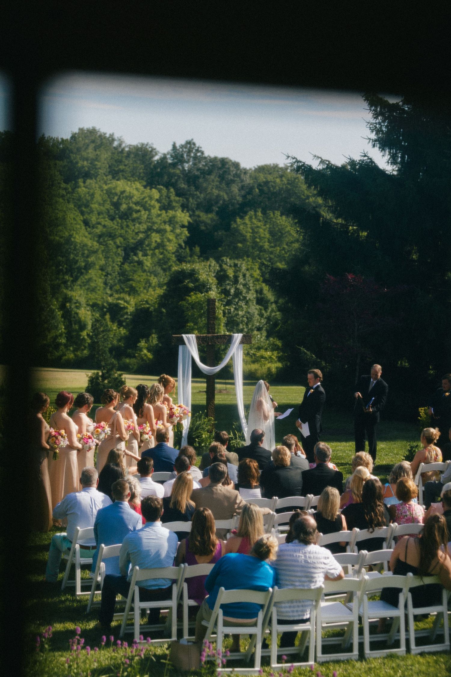 Outdoor wedding ceremony with guests seated in white chairs facing the altar on a green lawn.