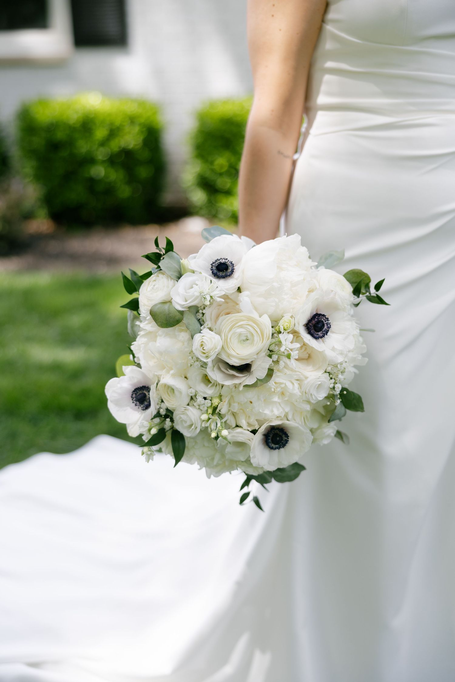 Bride holding a classic white bouquet of peonies, anemones, and ranunculus against her white gown.