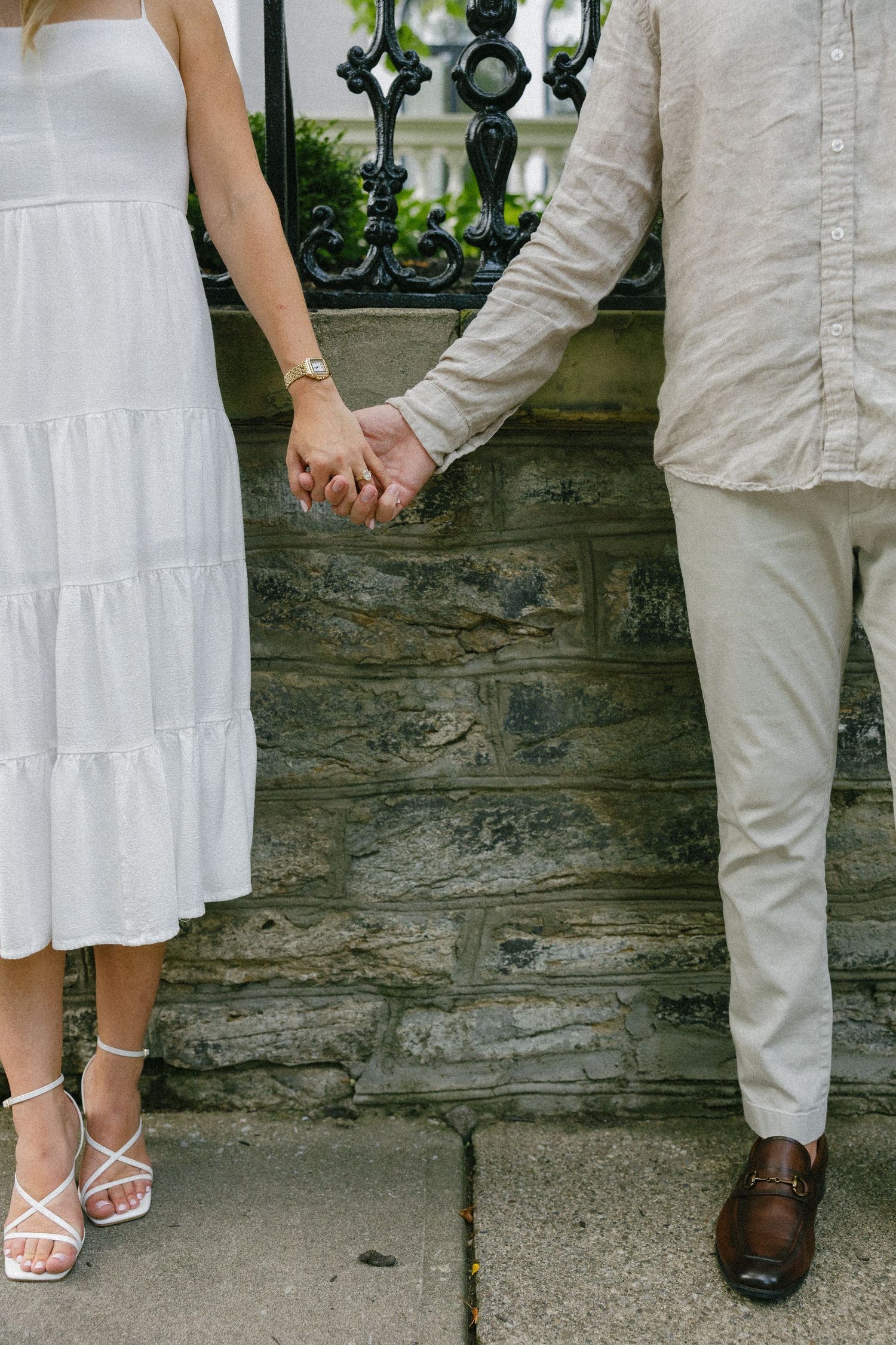 Close-up of couple holding hands, woman in white tiered dress with strappy heels, man in linen pants.
