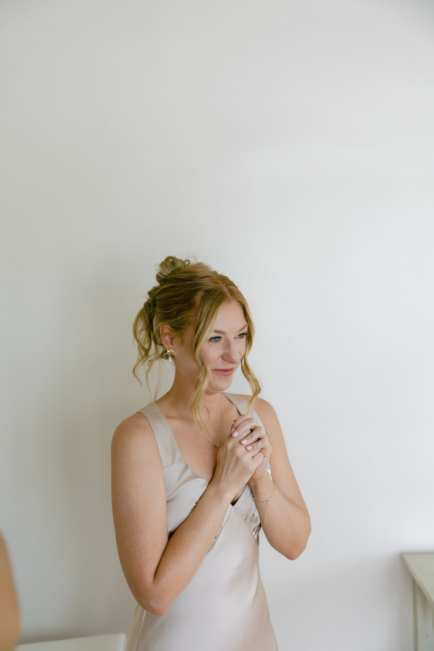 Bride in a silk slip dress clasping her hands together while getting ready on her wedding day.
