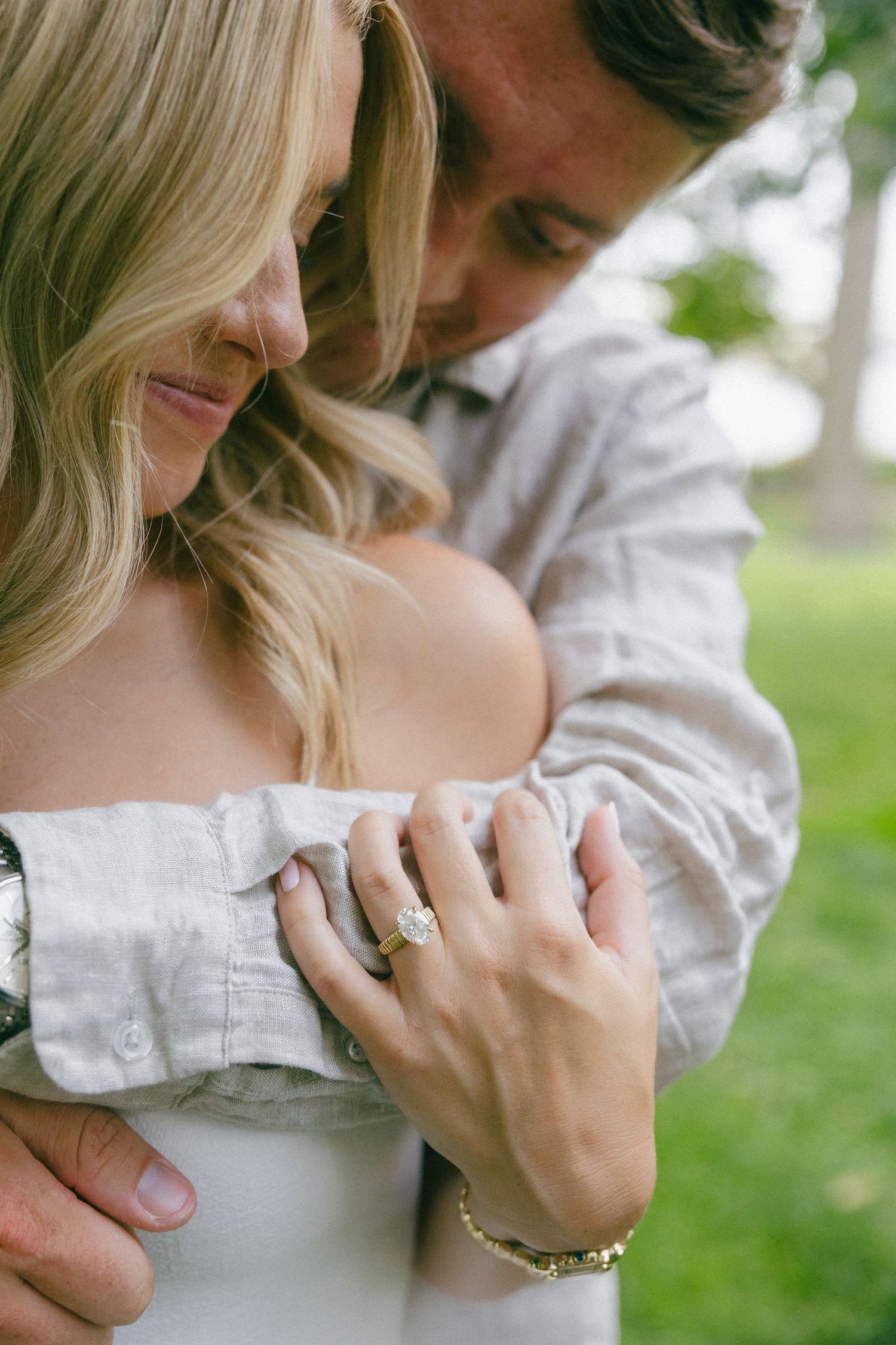 Man embracing woman from behind showing diamond engagement ring, captured in romantic close-up shot.