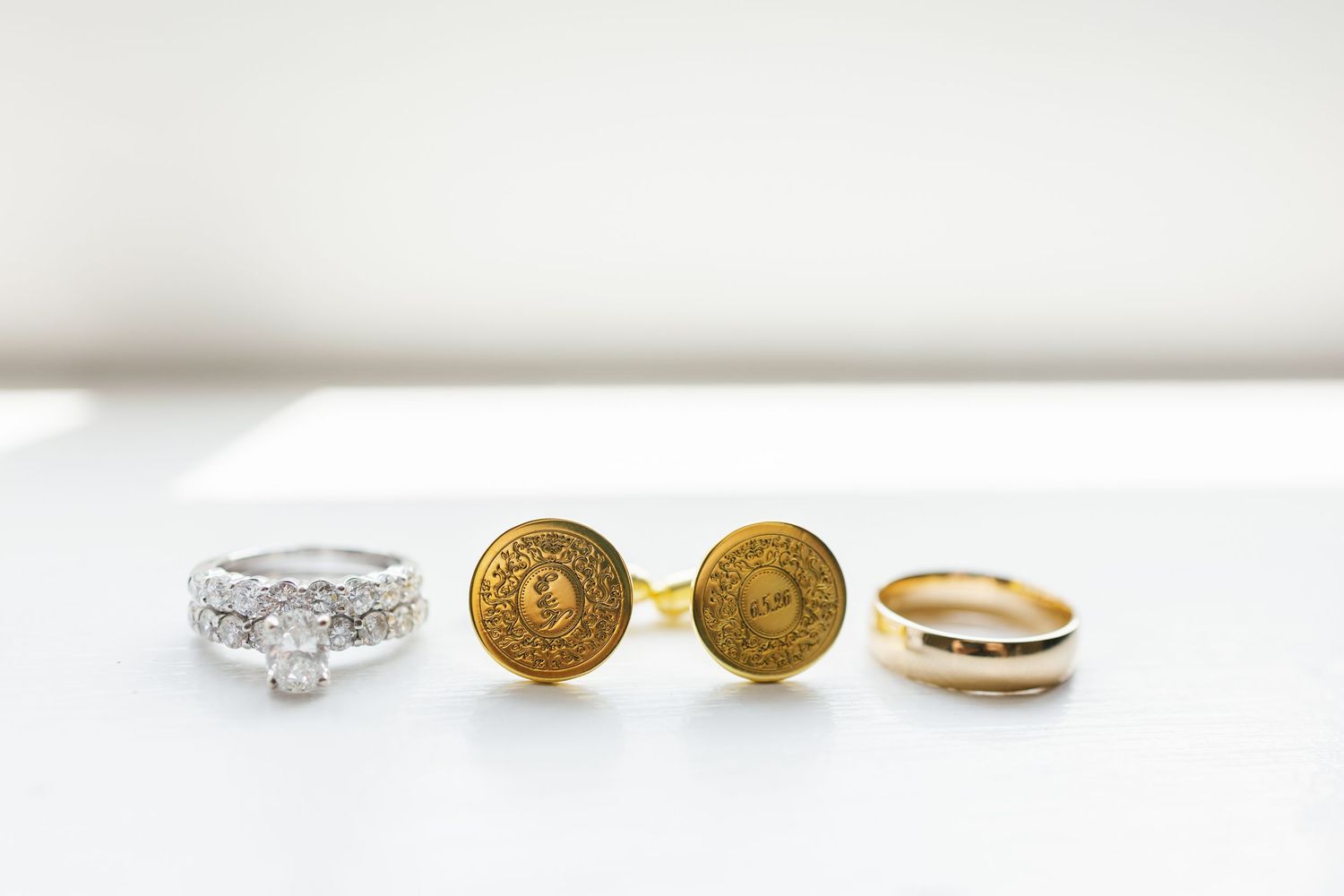 Wedding rings and gold cufflinks displayed on a white surface as elegant bridal accessories.