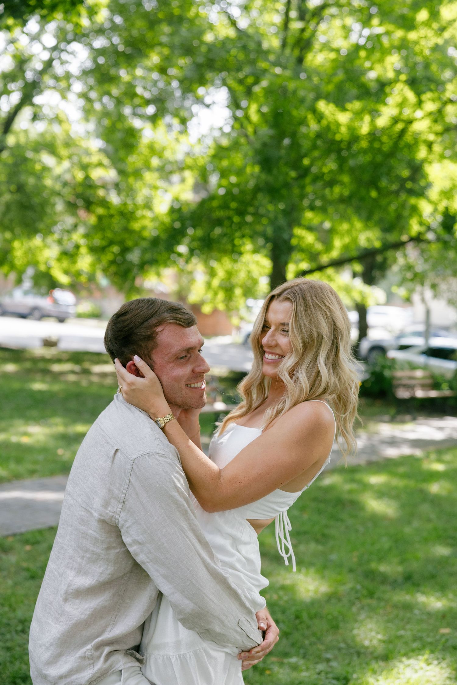 Joyful couple embracing outdoors in a lush green park, woman in white dress laughing with partner.