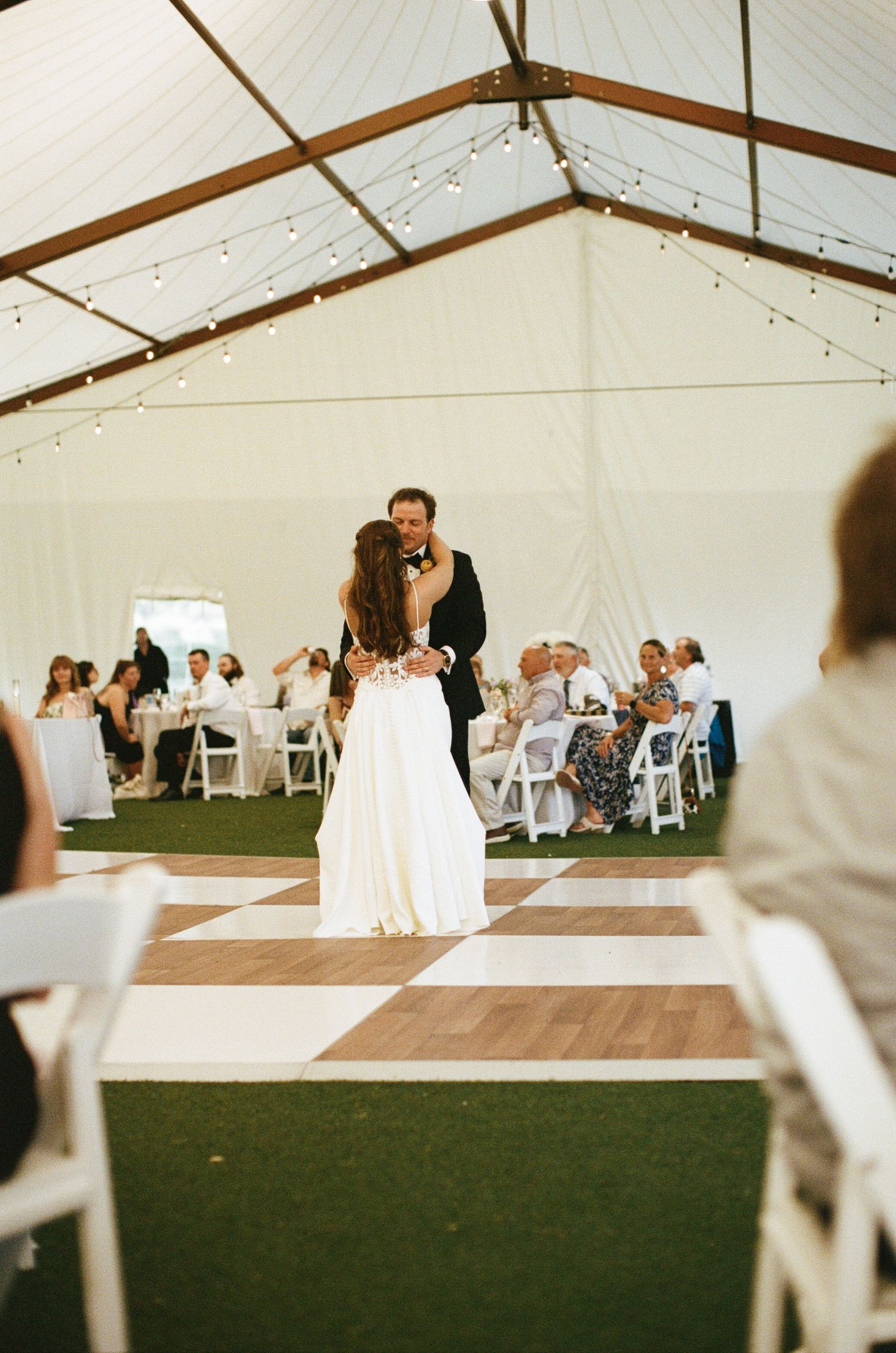 Bride and groom sharing first dance under a white tent with string lights and checkered dance floor. French Park photographer