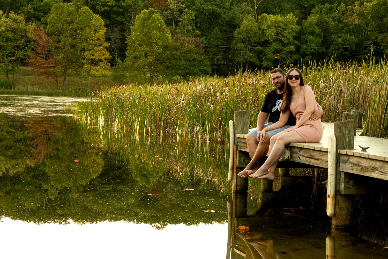 People relaxing on a wooden dock by a peaceful lake surrounded by trees.