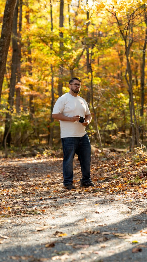 People walking on a sunlit autumn trail covered in fallen leaves.