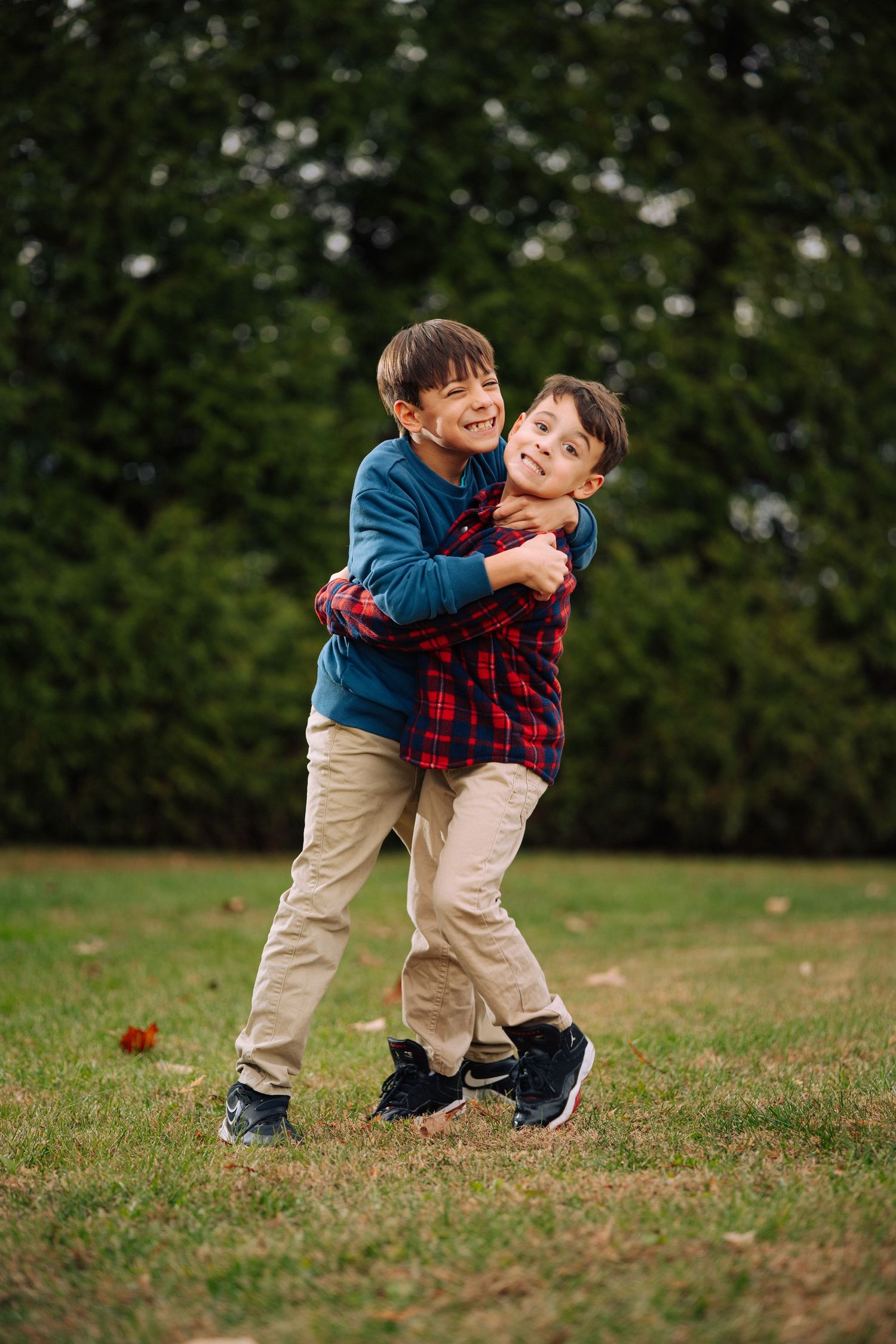 Two children in matching outfits playing together on grass during fall.