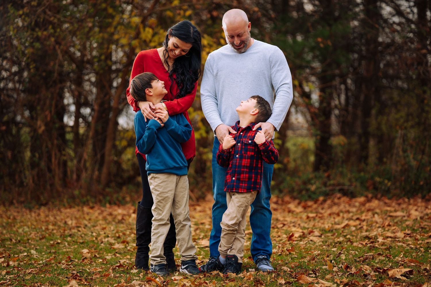 Family enjoys playtime together in park during fall season photoshoot.