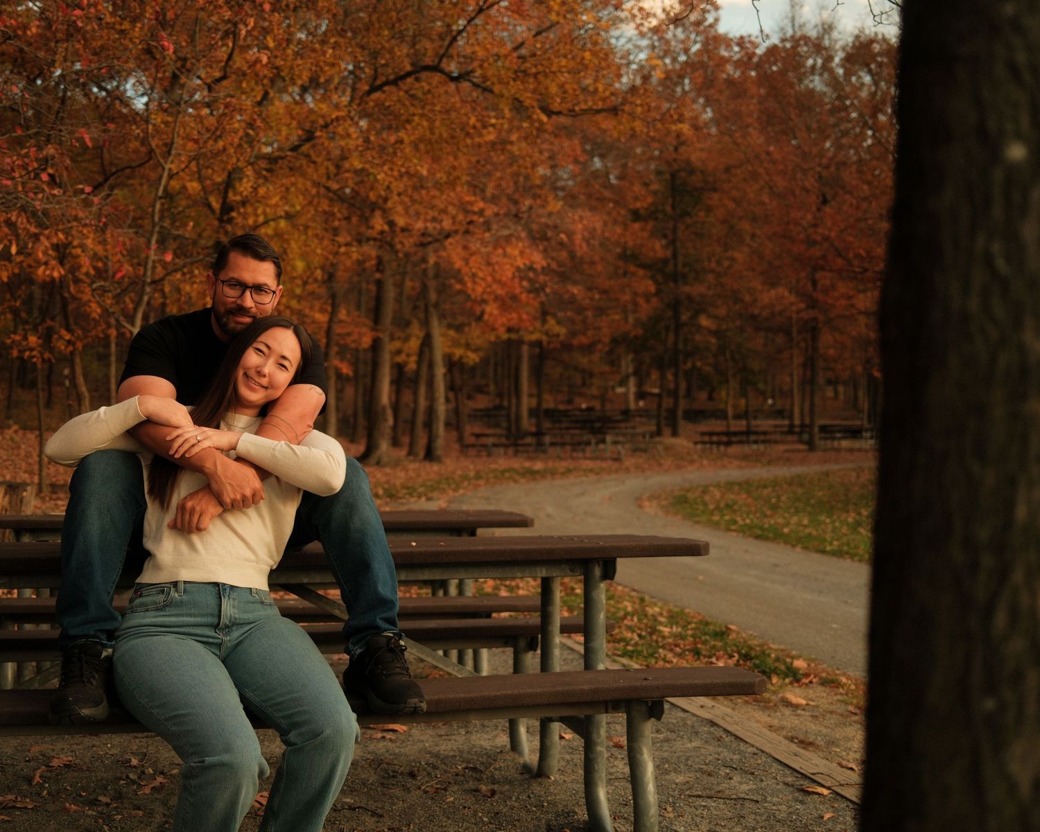People relaxing on picnic benches in a park during autumn.