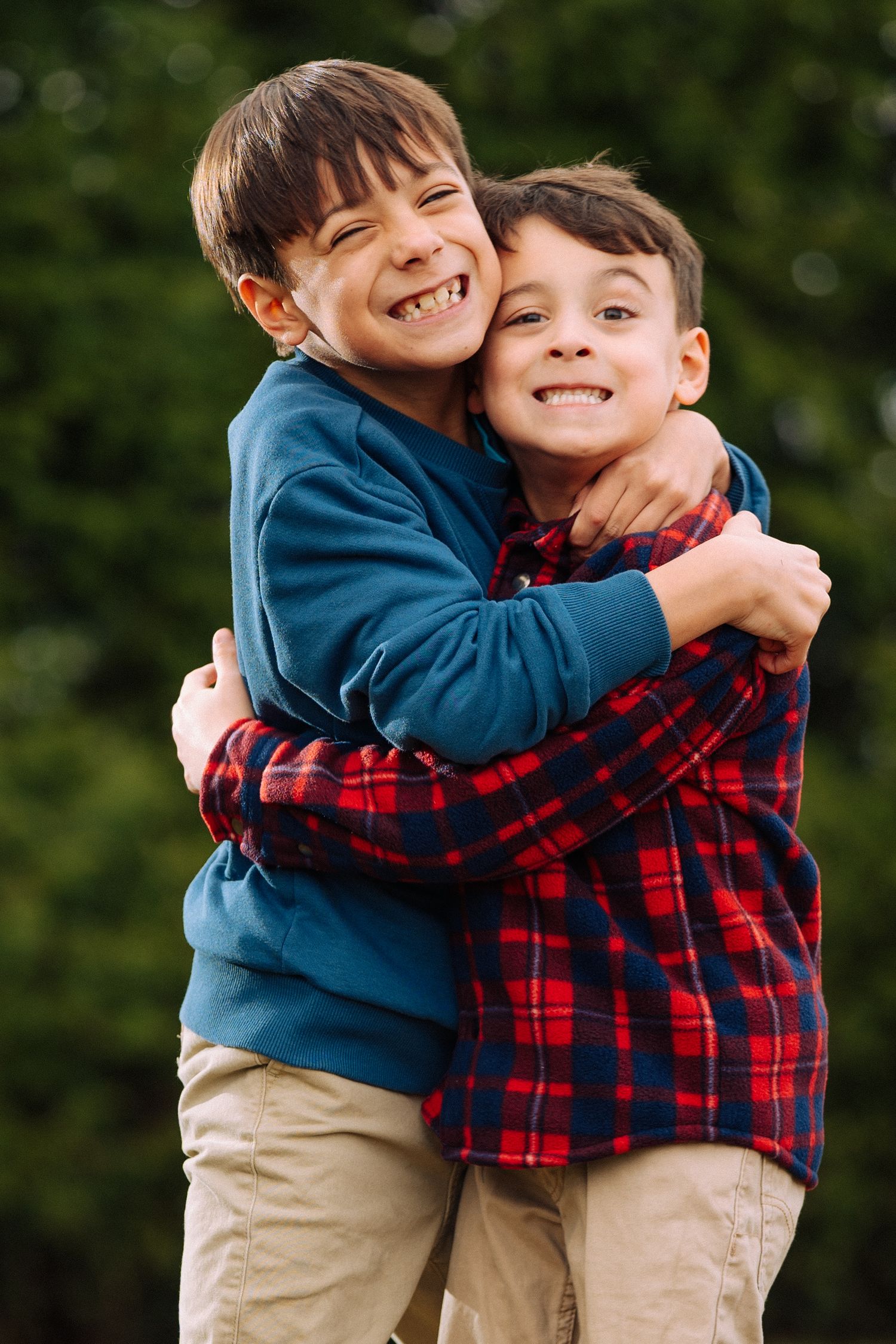 Two children share a playful hug while wearing casual clothing outdoors.