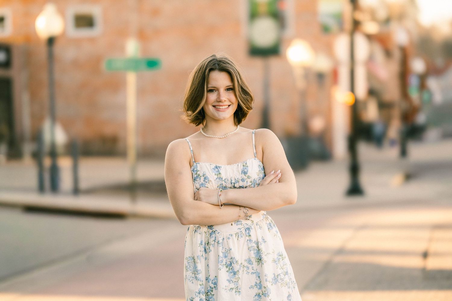 Senior portrait of a smiling young woman in a flowery timeless dress in front of golden hour Stillwater minnesota