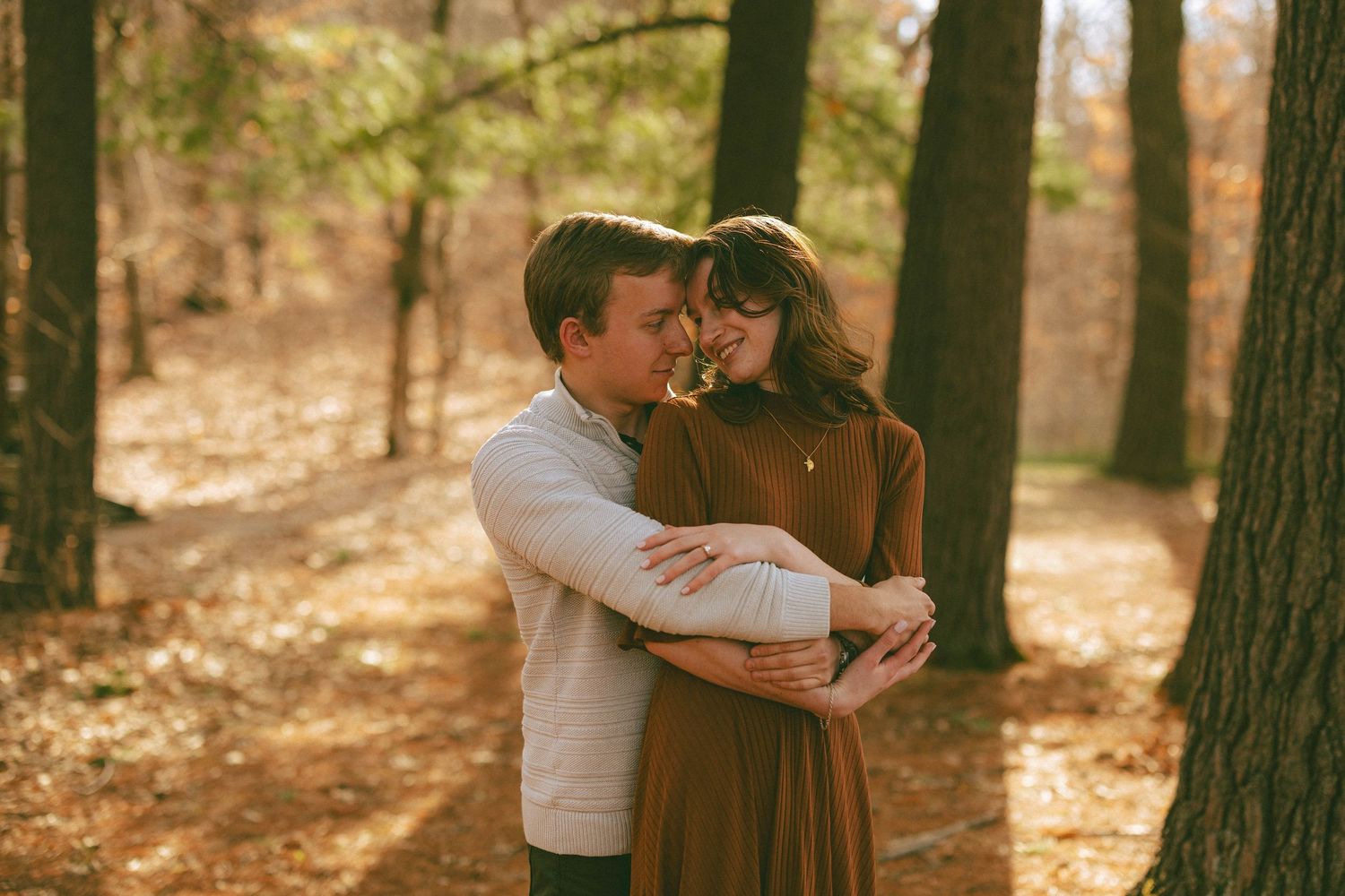 Couple sharing a tender embrace among autumn trees in a sunlit forest setting.